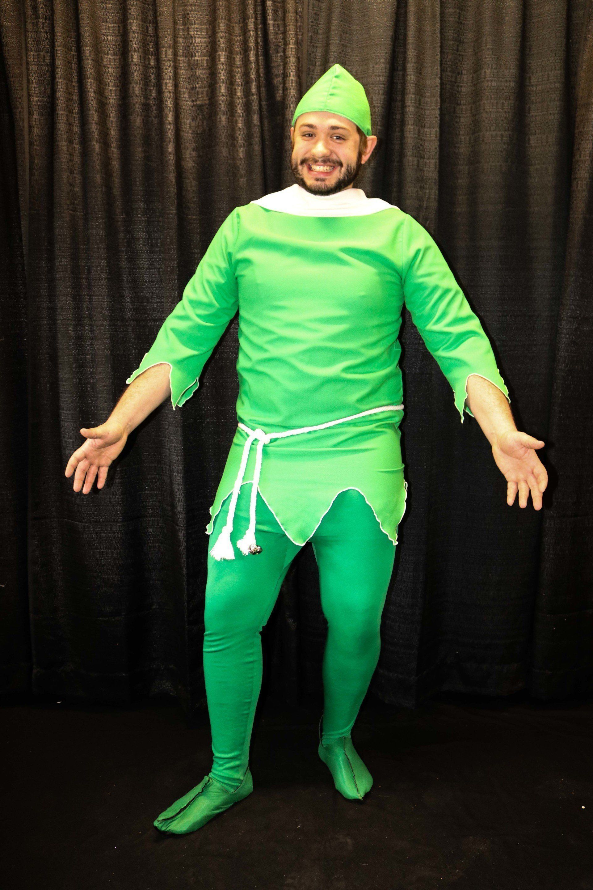 Man in green costume, arms outstretched, standing in front of black backdrop.