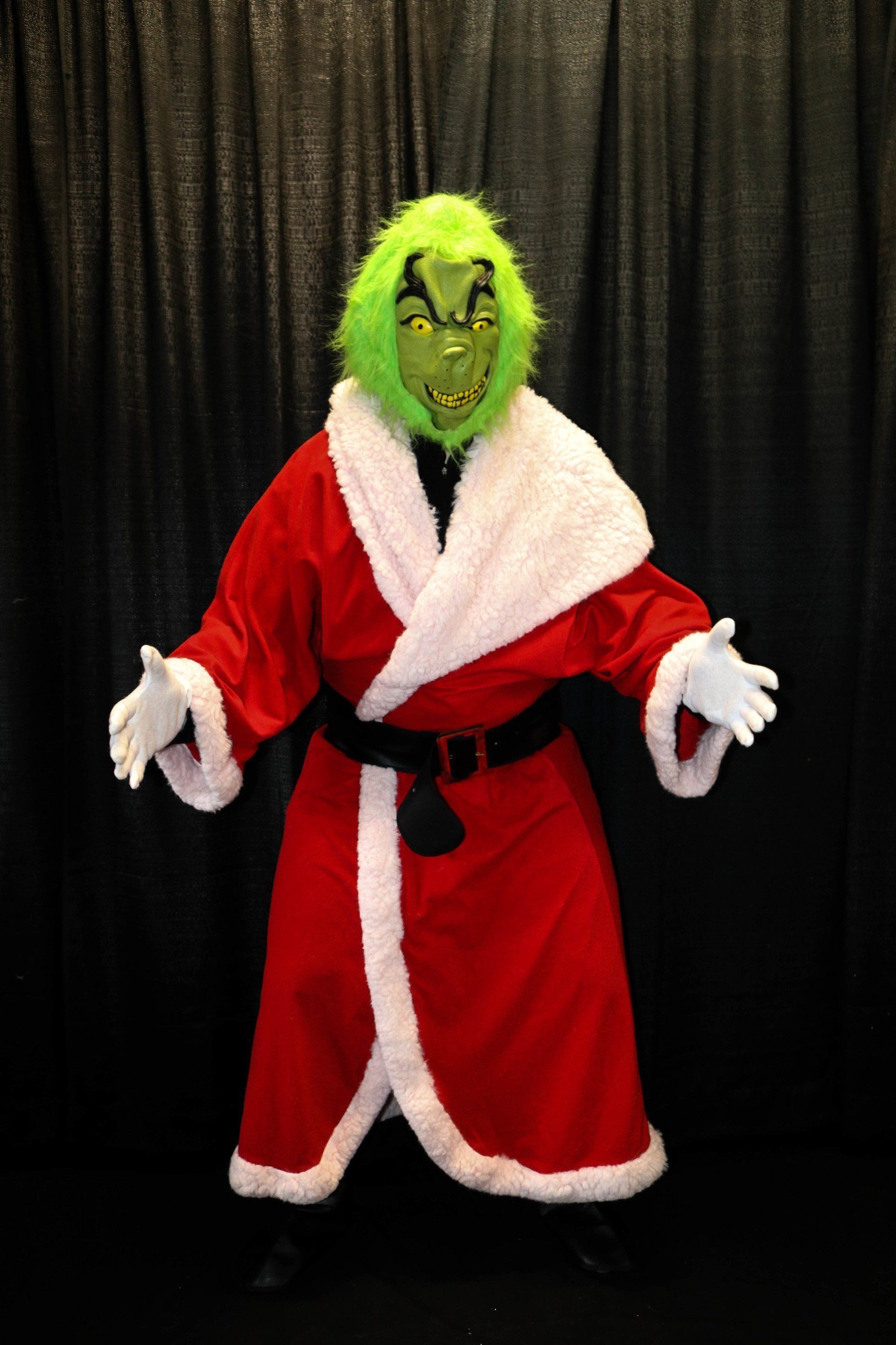 Grinch character wearing red Santa suit with white trim, green mask, black belt, and gloves.