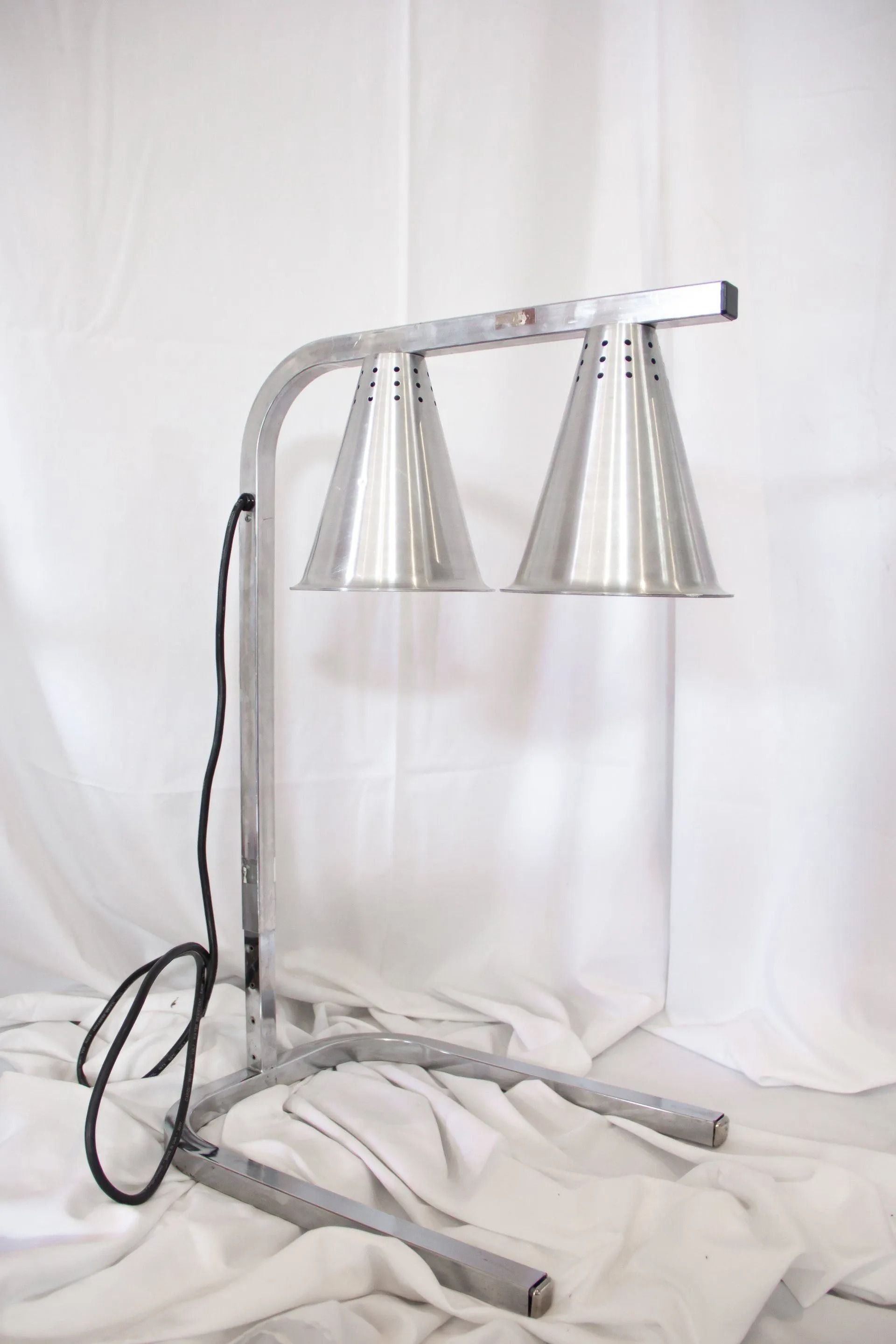 Silver food warming lamp with two conical shades, on a white background.