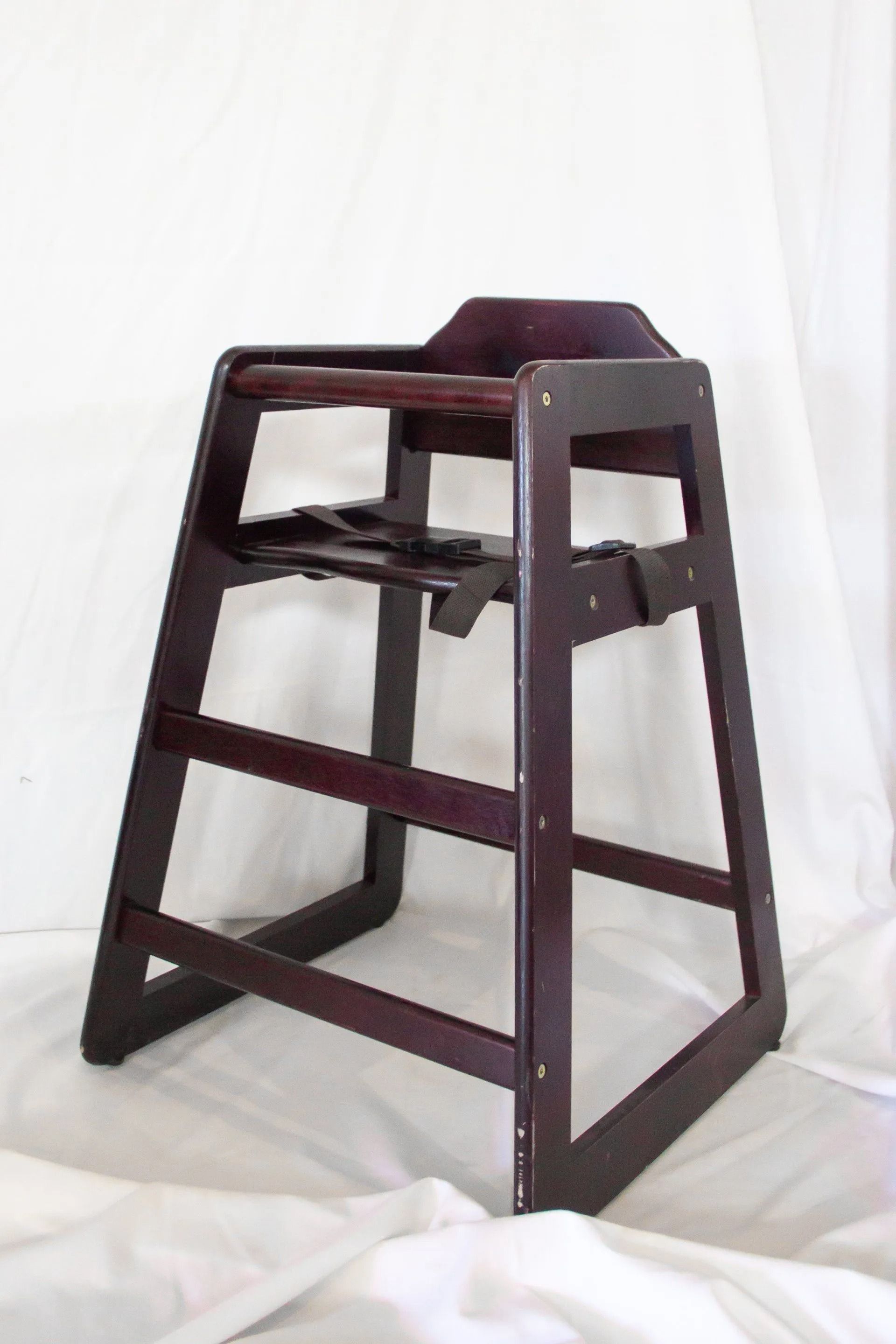 Dark wood high chair with a safety harness, against a white backdrop.