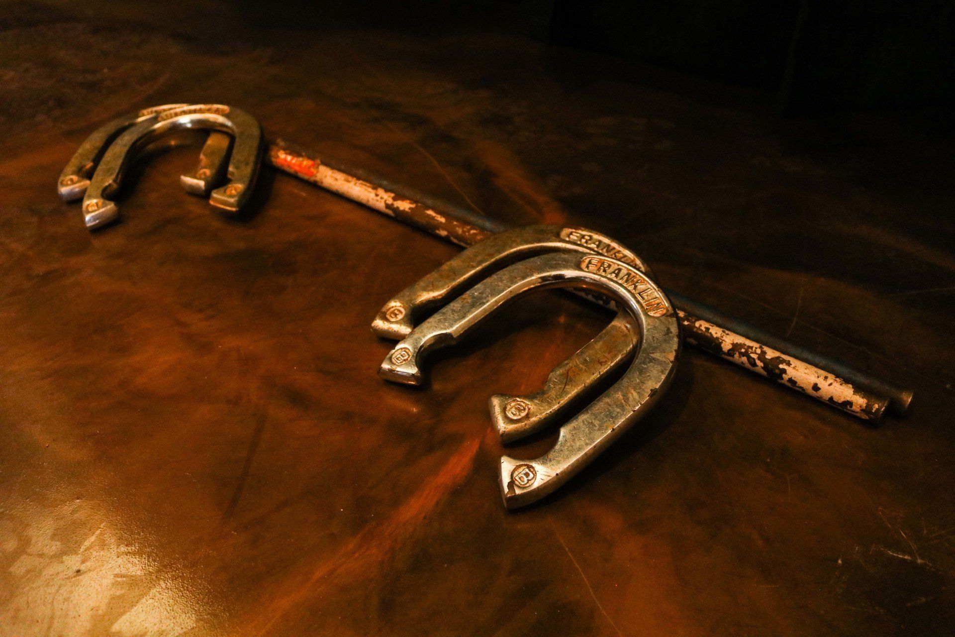 Two horseshoes connected by a rusty metal rod, lying on a brown leather surface.