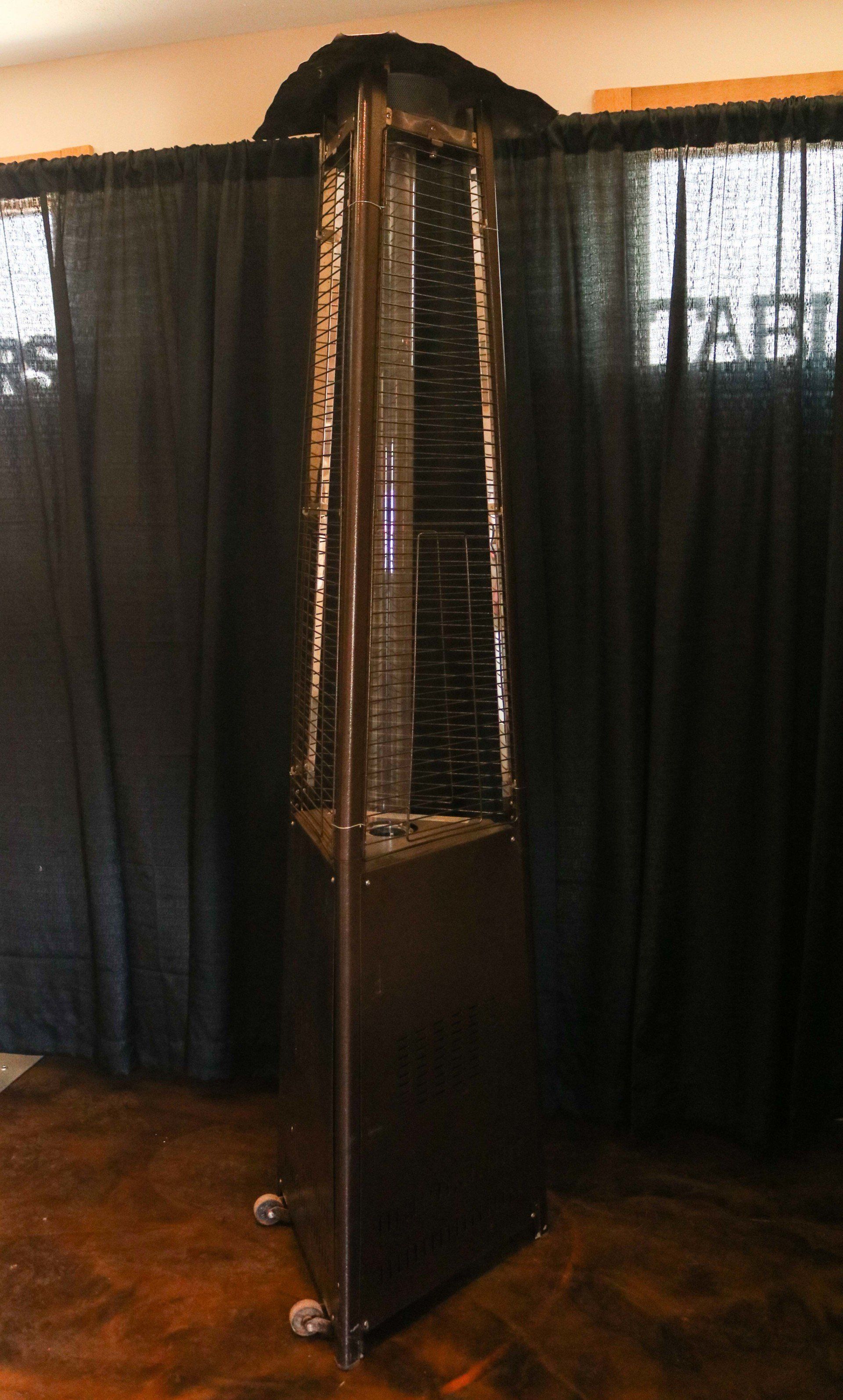 Tall, black outdoor patio heater on wheels, against a black backdrop.