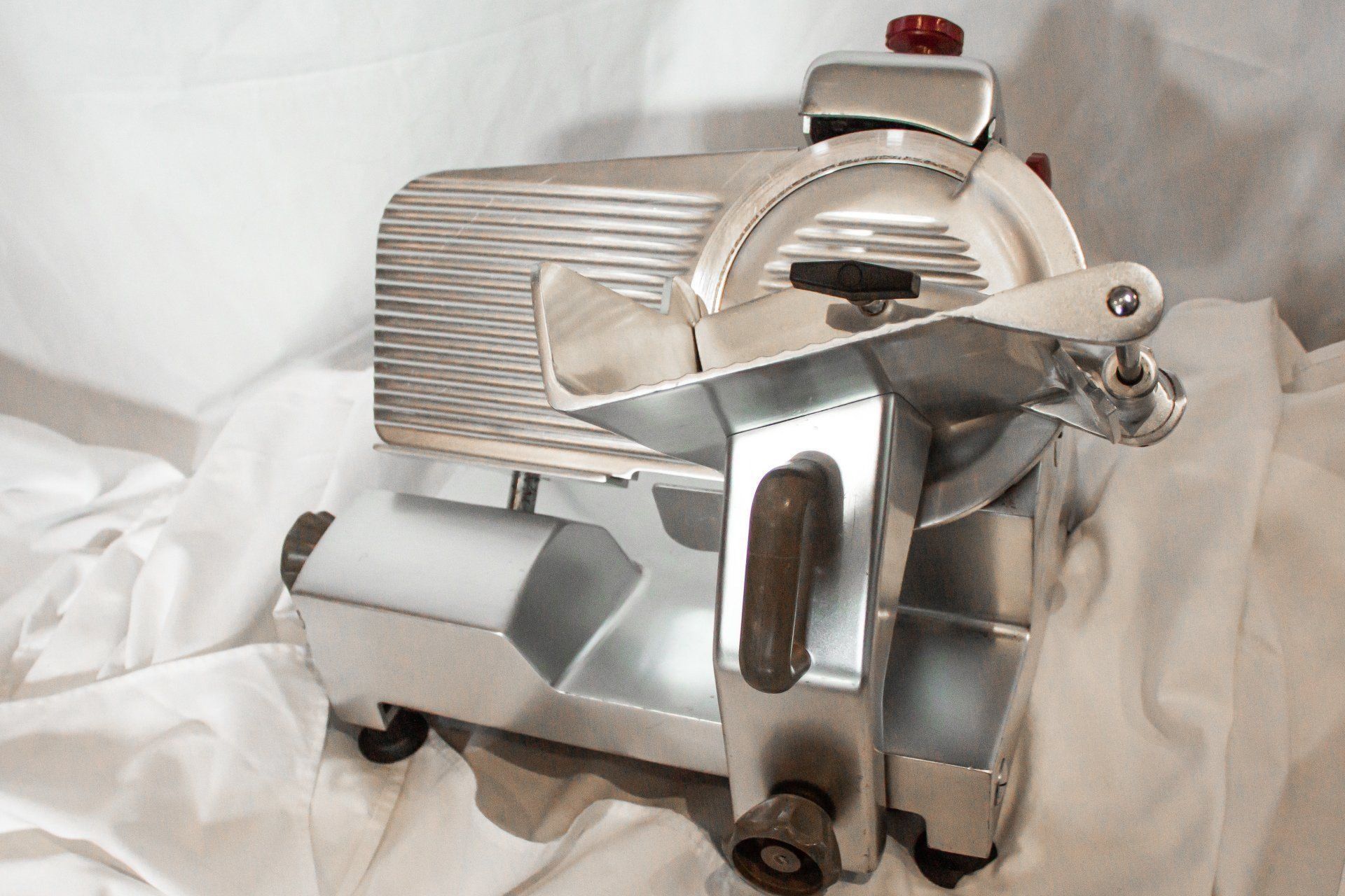 A silver commercial meat slicer on a white draped surface.