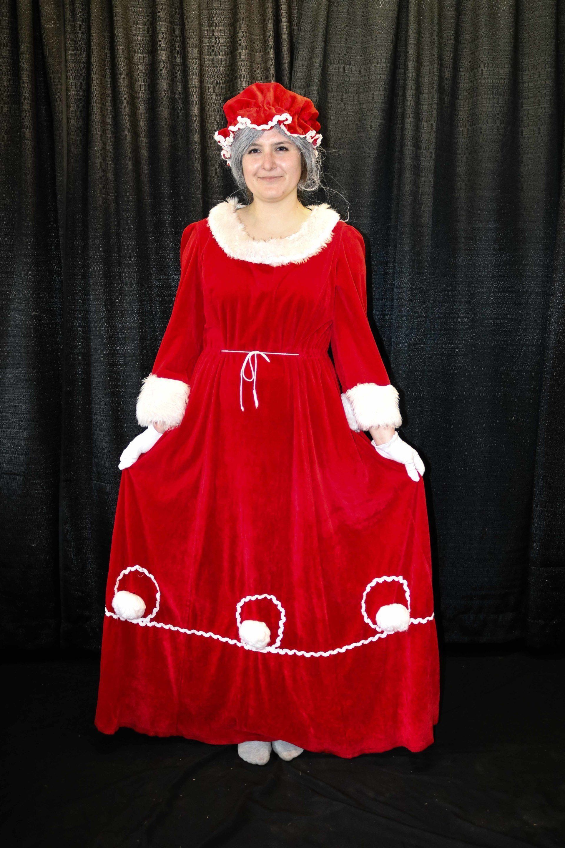 Woman in red Mrs. Claus costume with white trim, standing in front of a black backdrop.