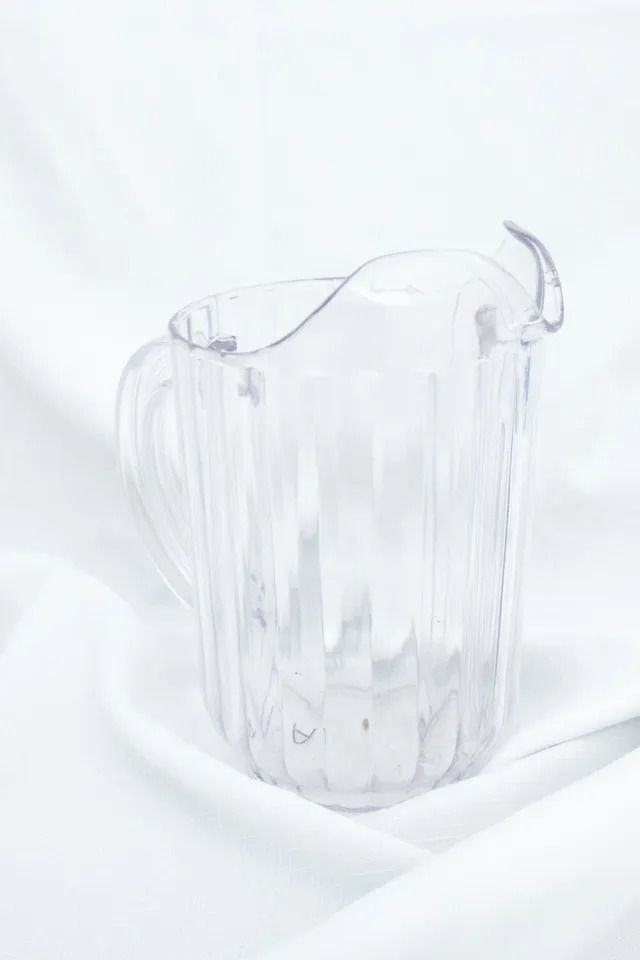Clear plastic pitcher with vertical ribs, sitting on white fabric.