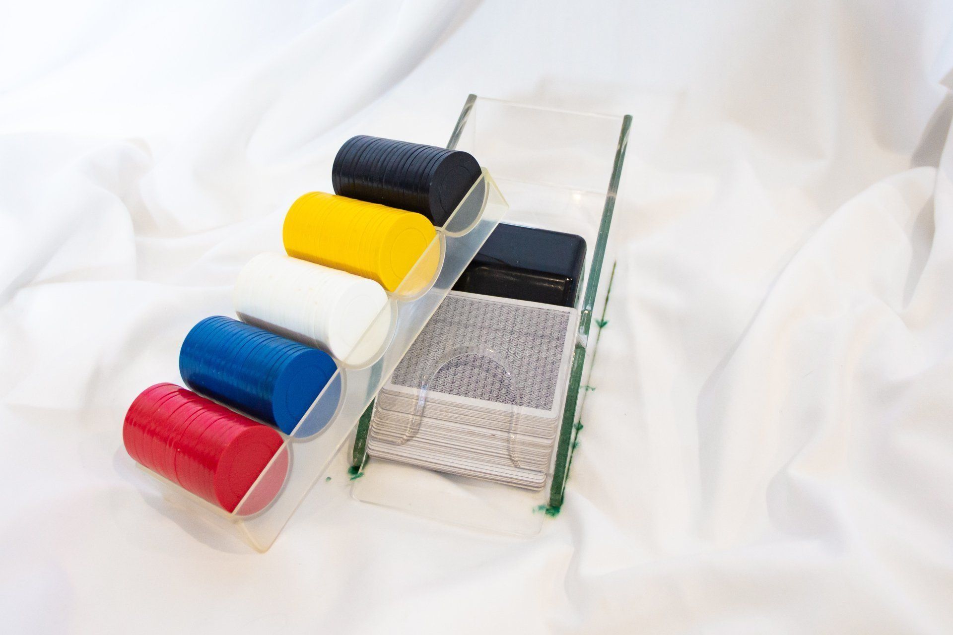 A clear acrylic organizer holding colorful cylindrical objects and knitted rectangles, set against a white fabric backdrop.