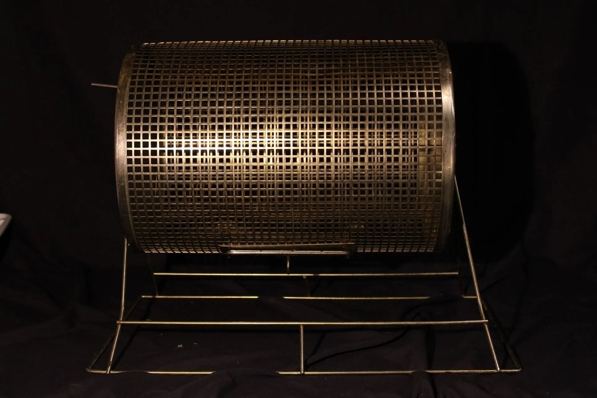 Metal lottery drum on a wire stand against a black background.