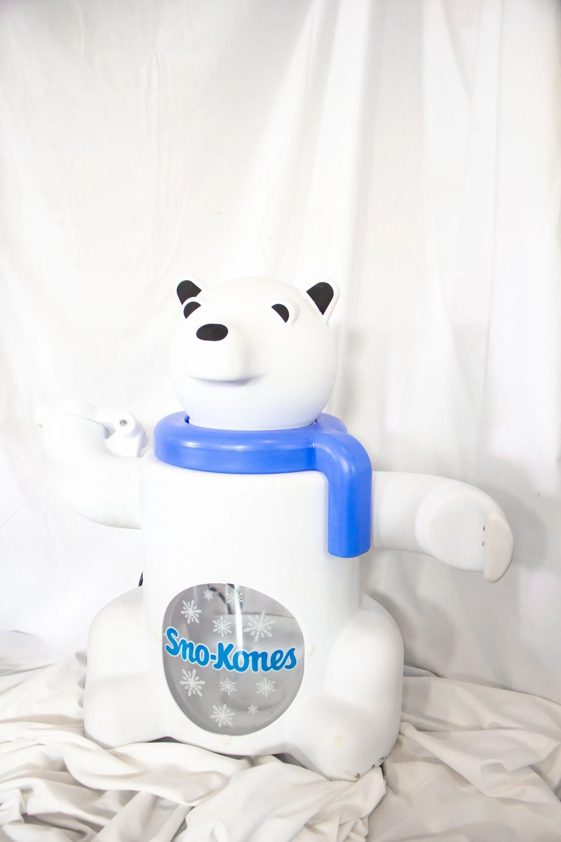 White polar bear-shaped Sno-Kones sign with blue scarf, black ears, and a snow-themed window.