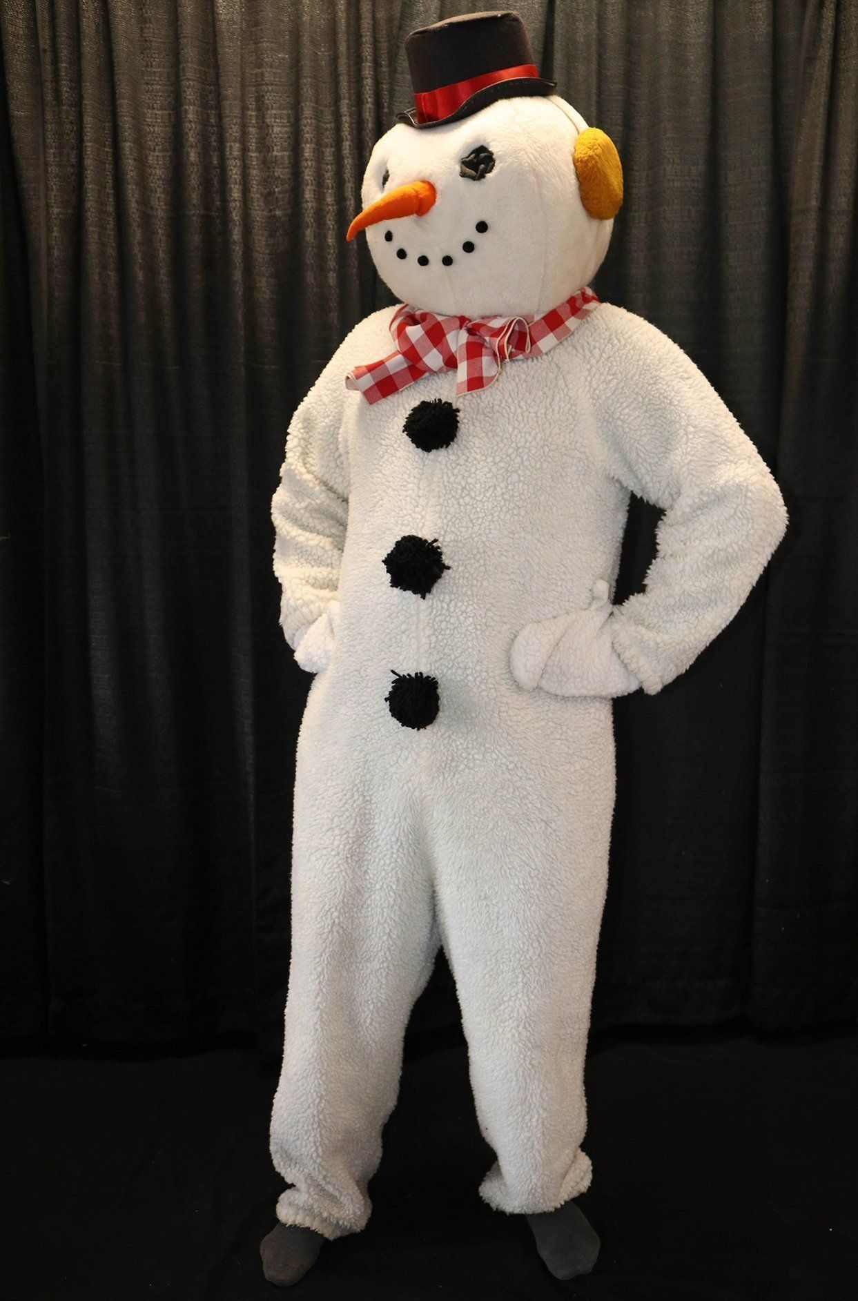 Snowman costume, black hat, carrot nose, red scarf, hands on hips.
