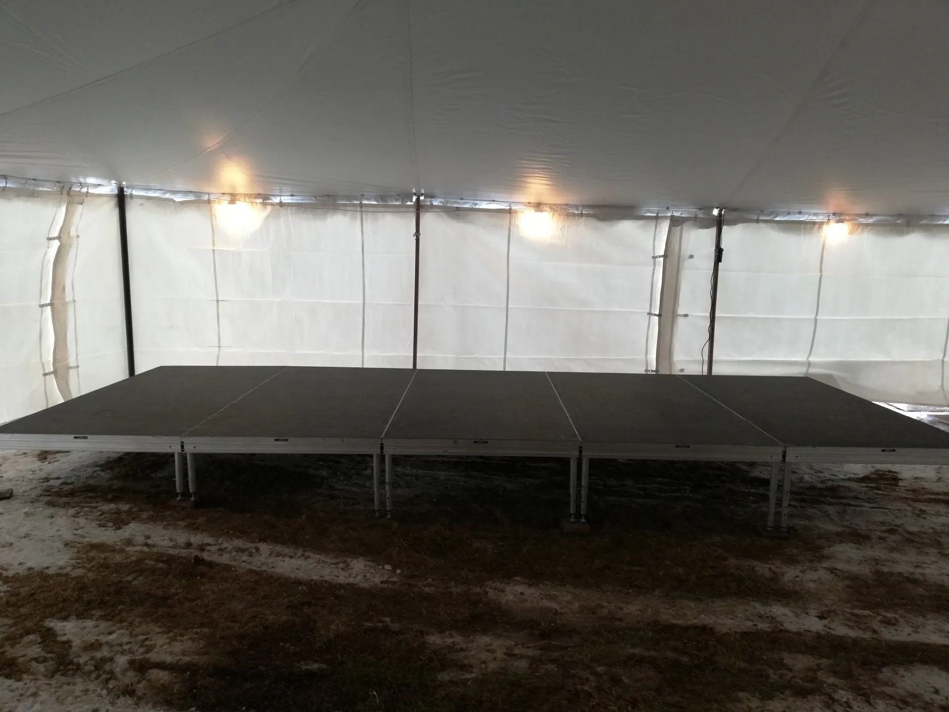Solar panels inside a structure, supported by metal legs, on a dirt floor.