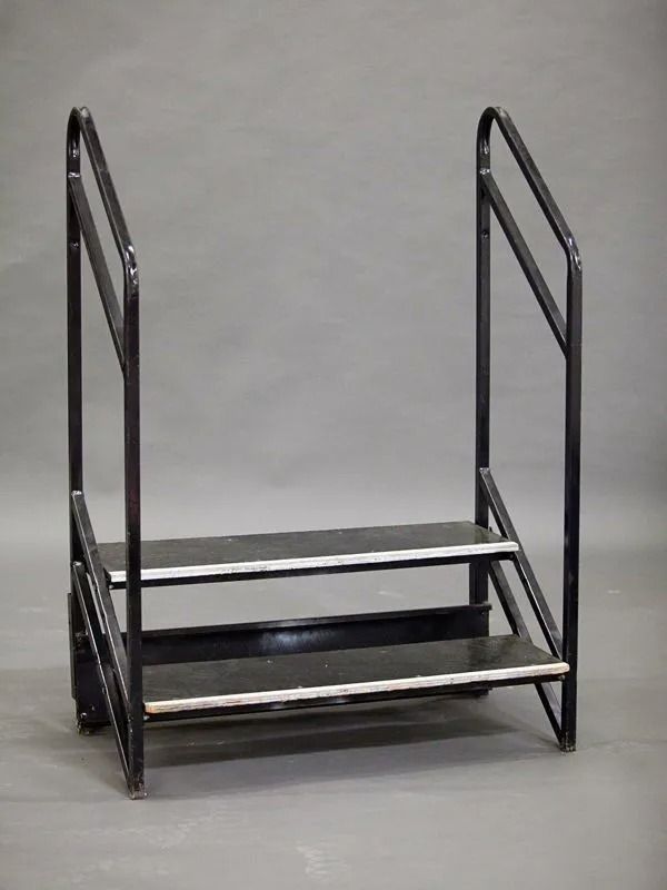 Black metal two-step staircase with handrails, against a gray background.