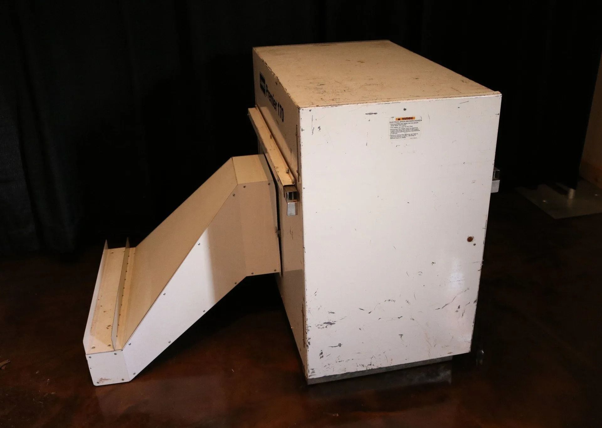 White industrial machine with a sloped chute, against a dark backdrop.