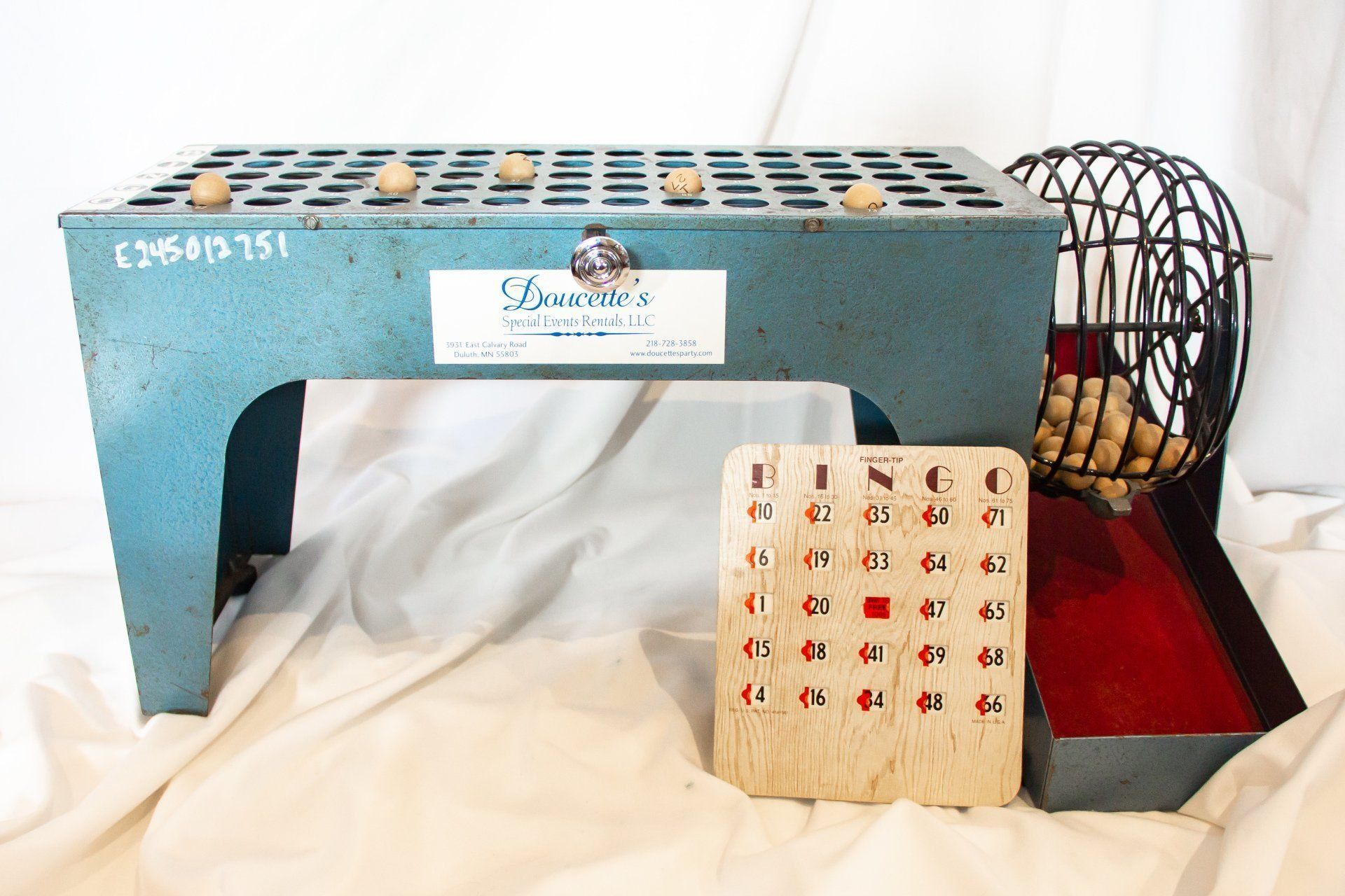 Blue bingo cage with balls, card, and metal rolling cage, on white fabric.