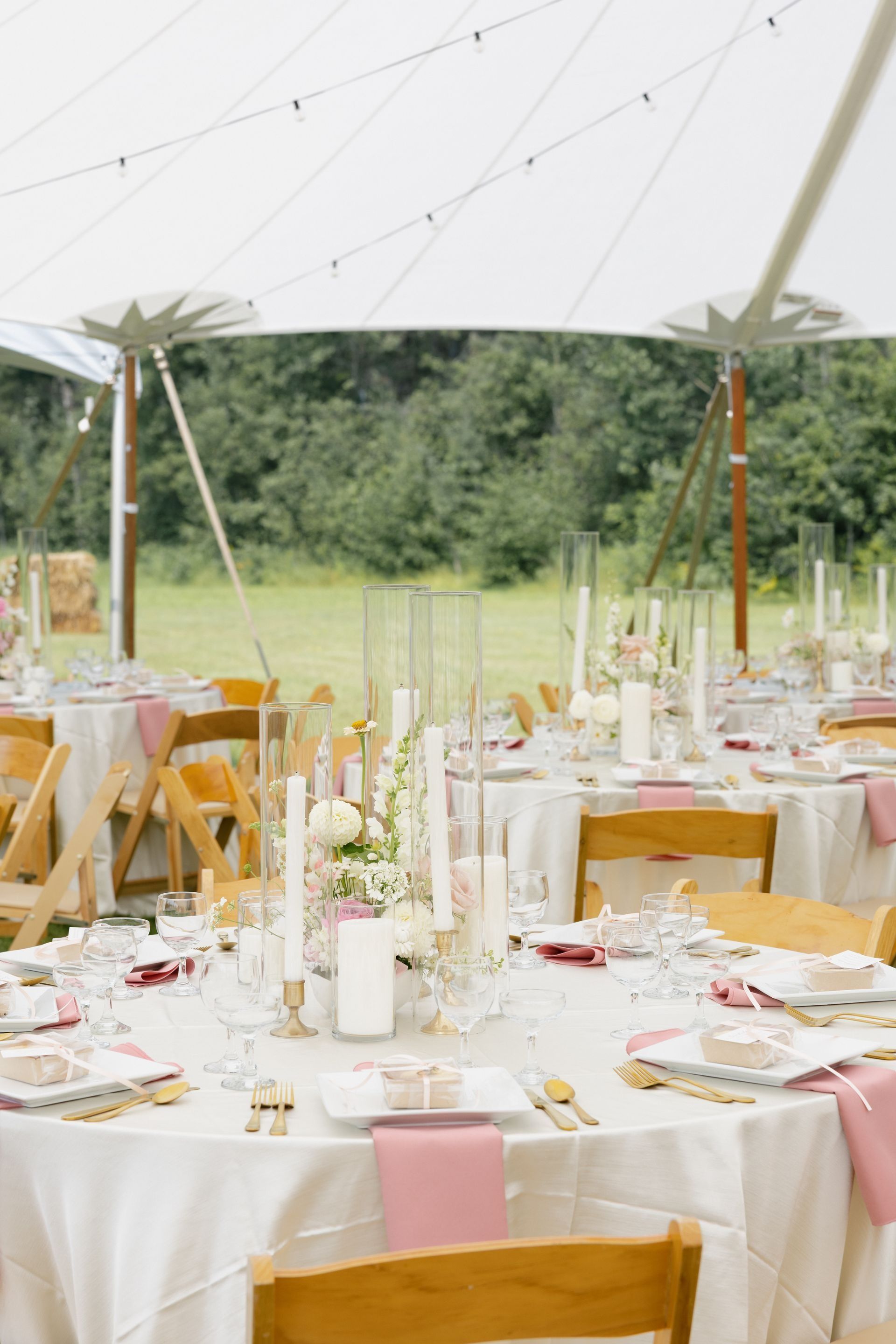 Wedding reception tables set under a white tent; round tables with pink napkins, flowers, and candles.