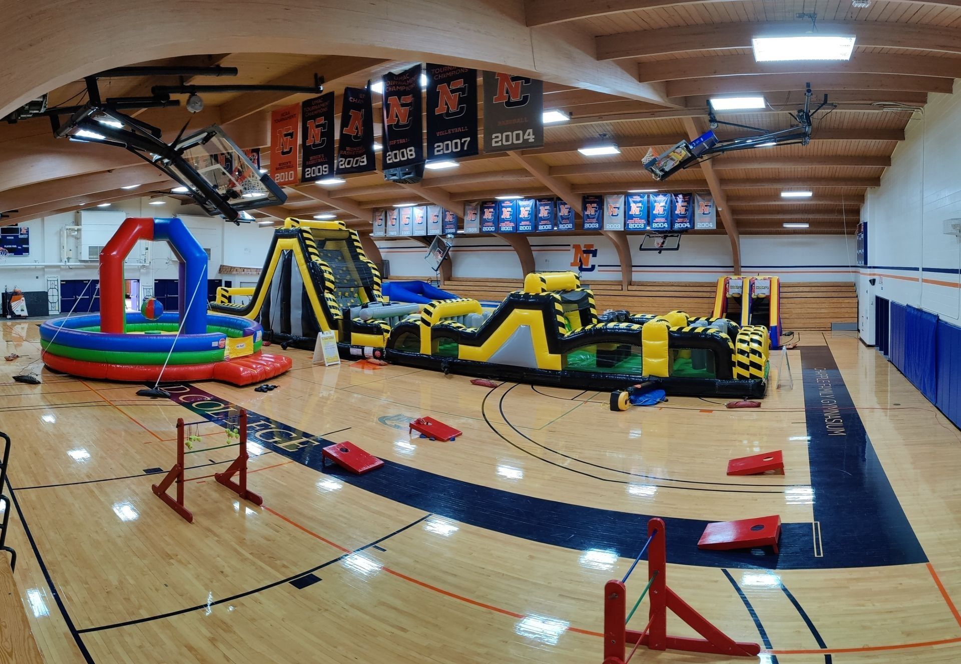 Indoor gymnasium with inflatable obstacle course set up on the wooden floor.