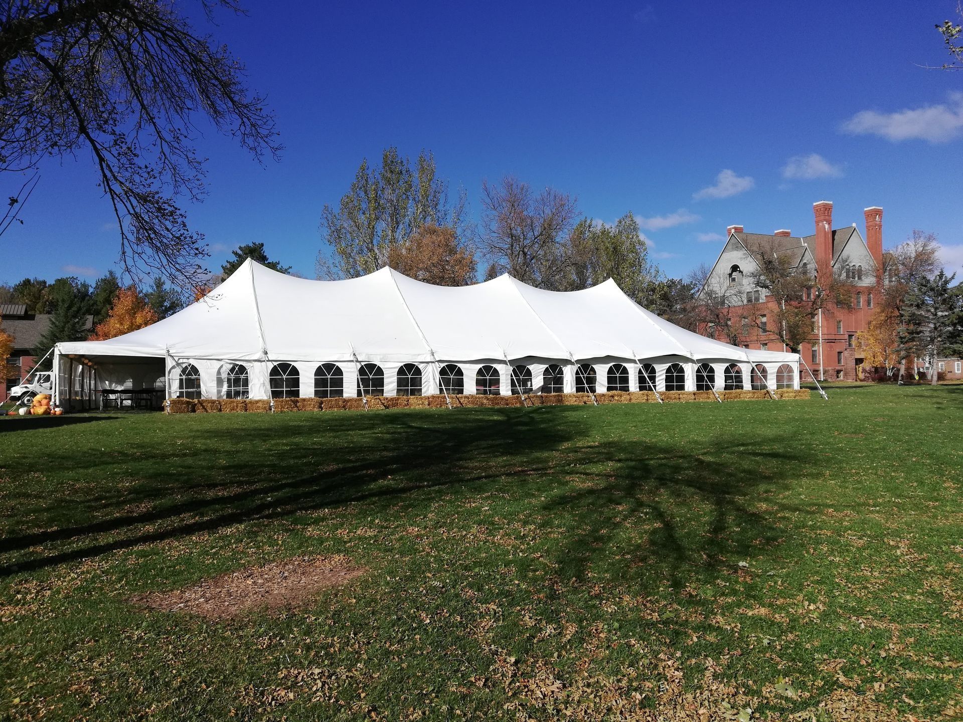 White event tent set up on a grassy lawn with a building in the background. Bright blue sky overhead.