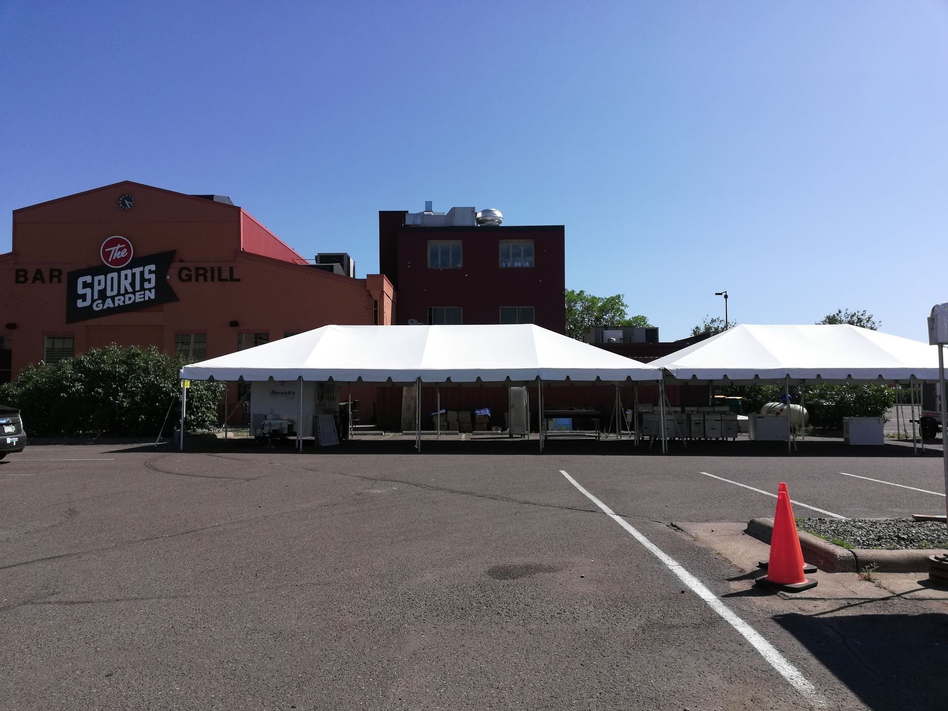 Two white tents set up in a parking lot in front of a sports bar on a sunny day.