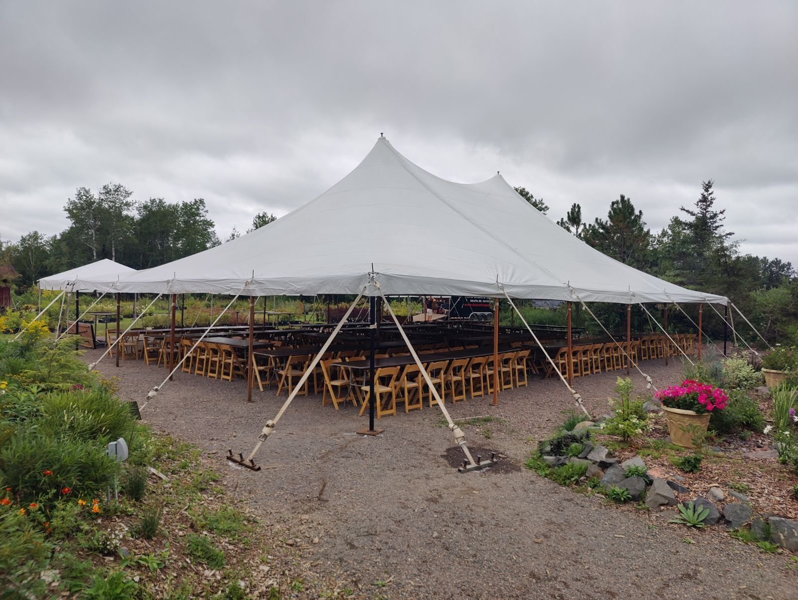 White tent set up with chairs and tables in a garden setting on a gravel surface.