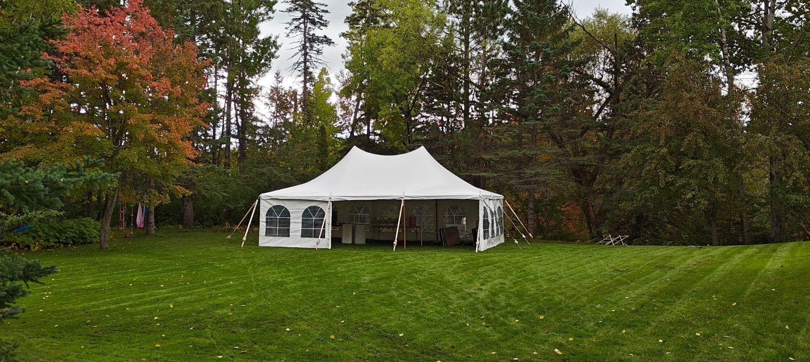 White tent set up on a grassy lawn, surrounded by trees with colorful fall foliage.