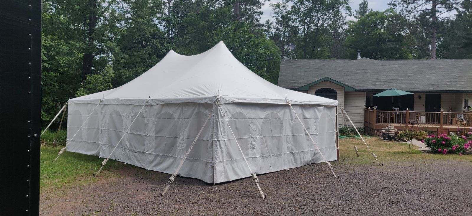 White tent set up on gravel, near a building with a deck and surrounding trees.