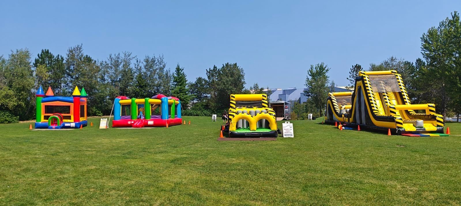 Four colorful inflatable bounce houses on a grassy field under a blue sky.
