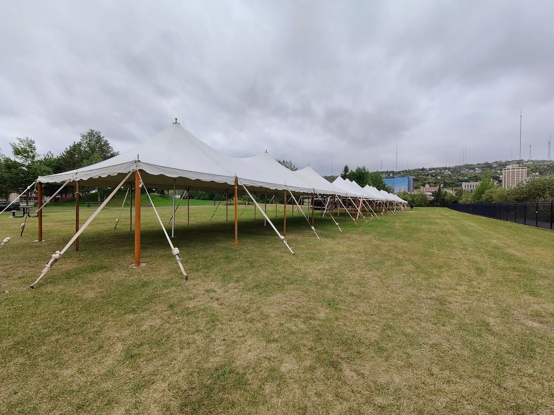 White tents on a grassy field under a cloudy sky. Wooden poles support the tent fabric.