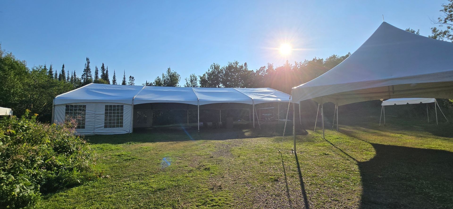Two white tents in a grassy outdoor setting, with sunlight shining brightly.