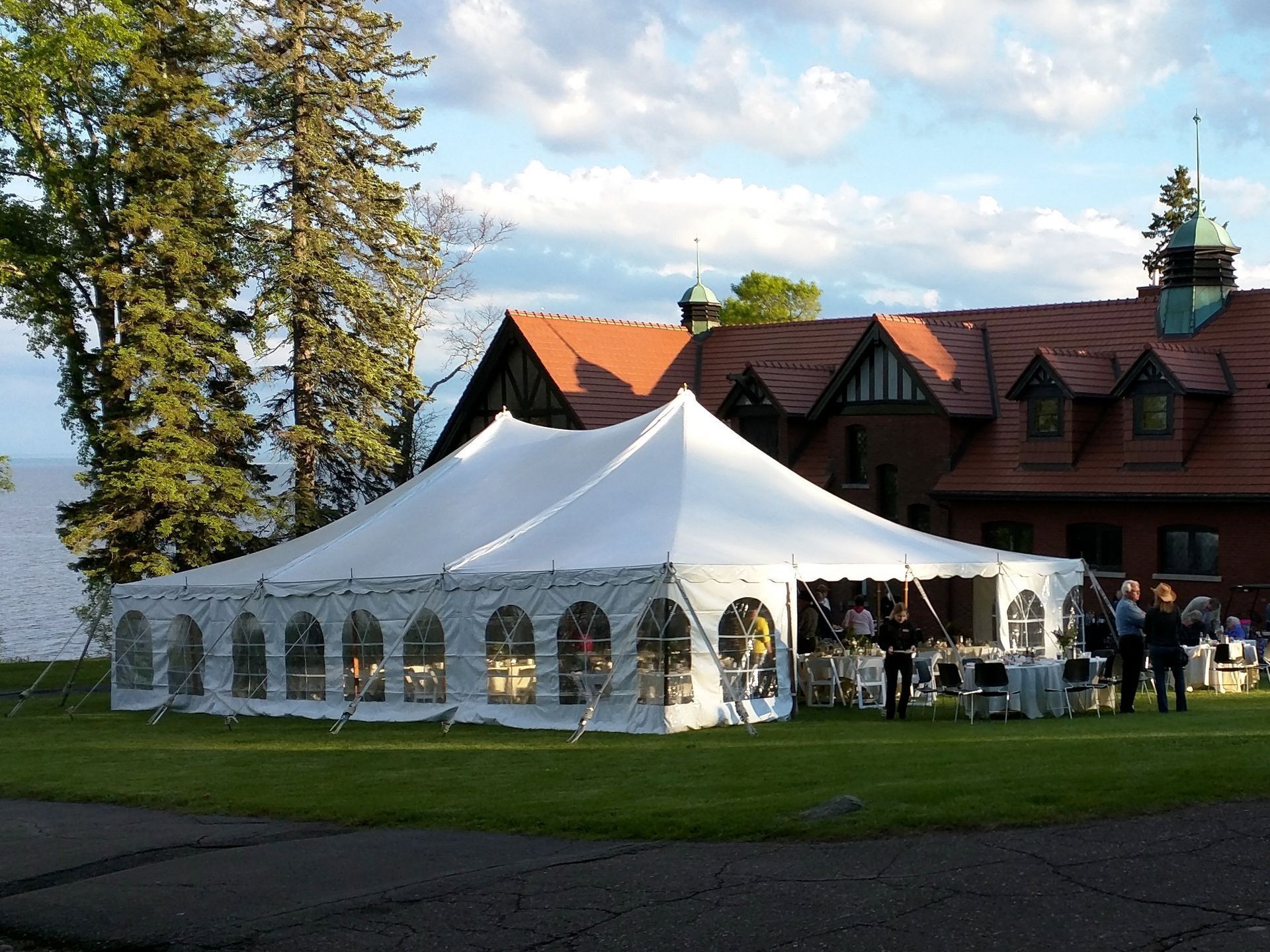 White tent set up on a lawn, with a brick building in the background. People are gathered near tables.