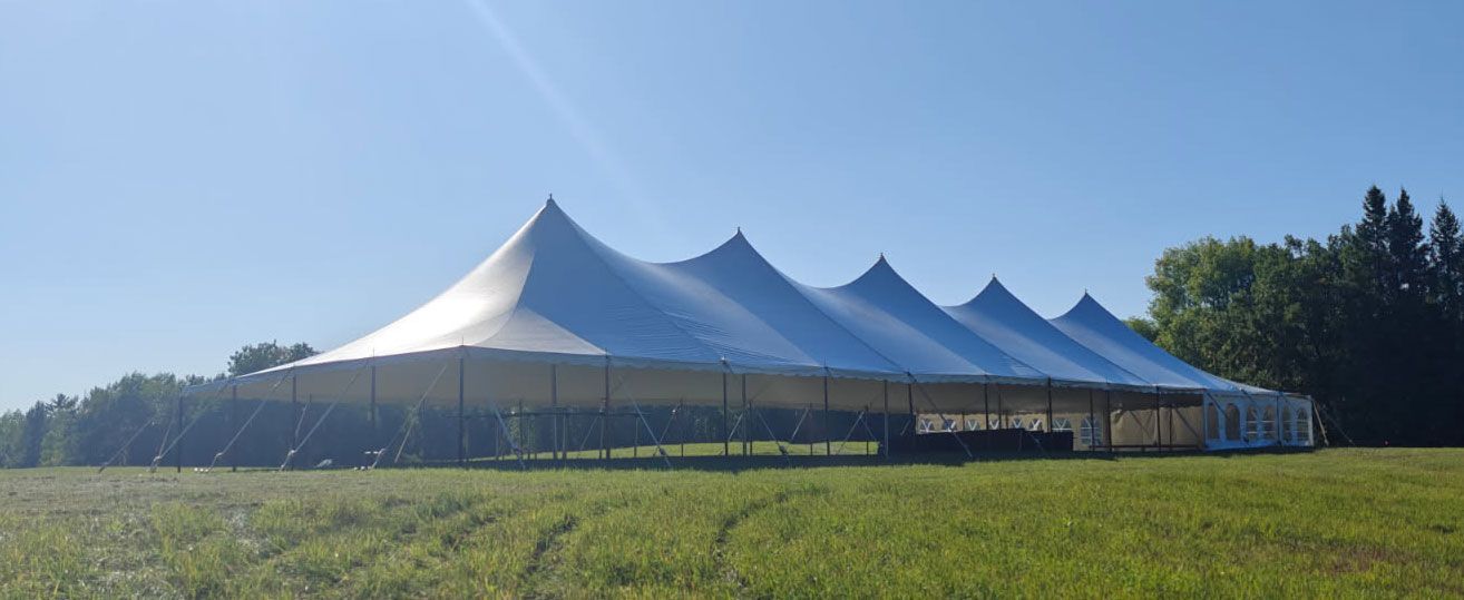 A large white tent with pointed peaks in a grassy field on a sunny day.