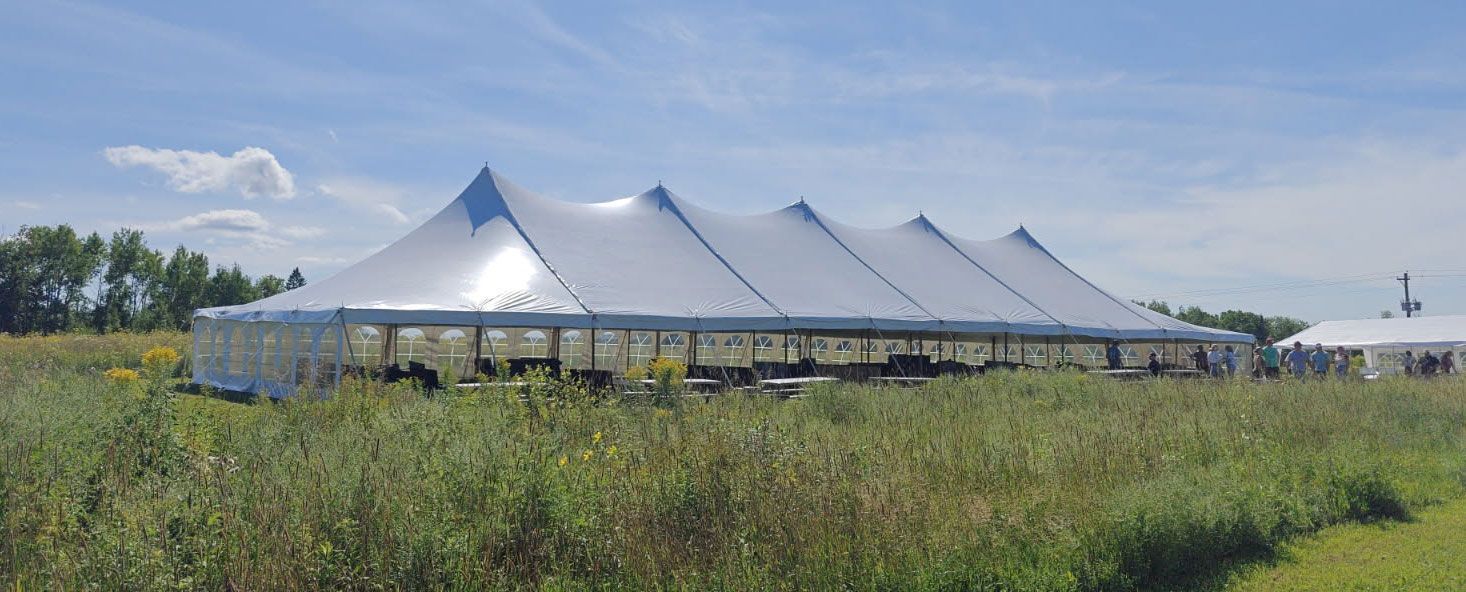 Large white event tent in a grassy field under a blue sky.