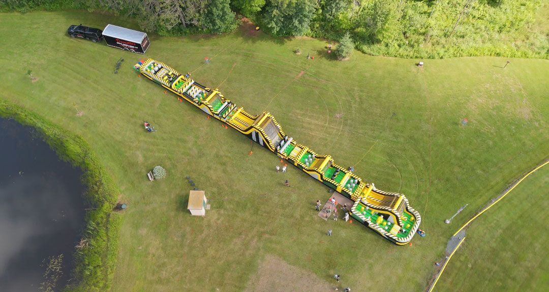 Aerial view of a long line of connected, brightly colored playground structures on grassy field near water.