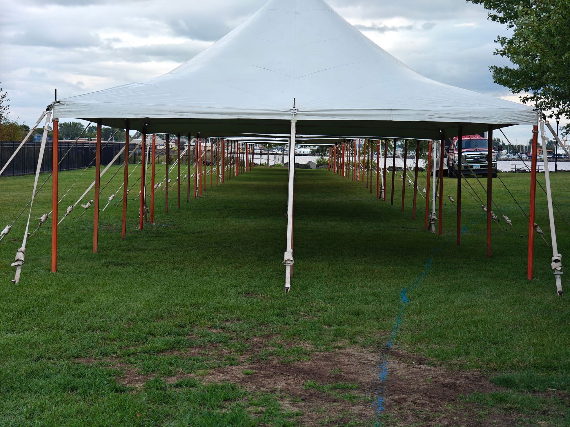 Large white tent erected on green grass, supported by orange poles.