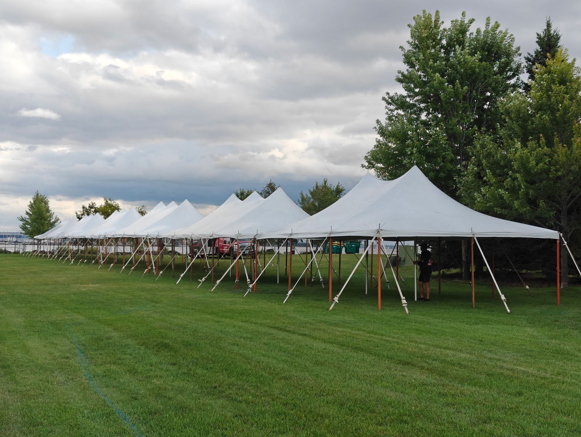 Row of white tents on green grass under a cloudy sky.