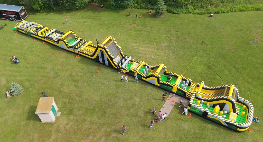 Aerial view of a long inflatable obstacle course with participants on a grassy field.