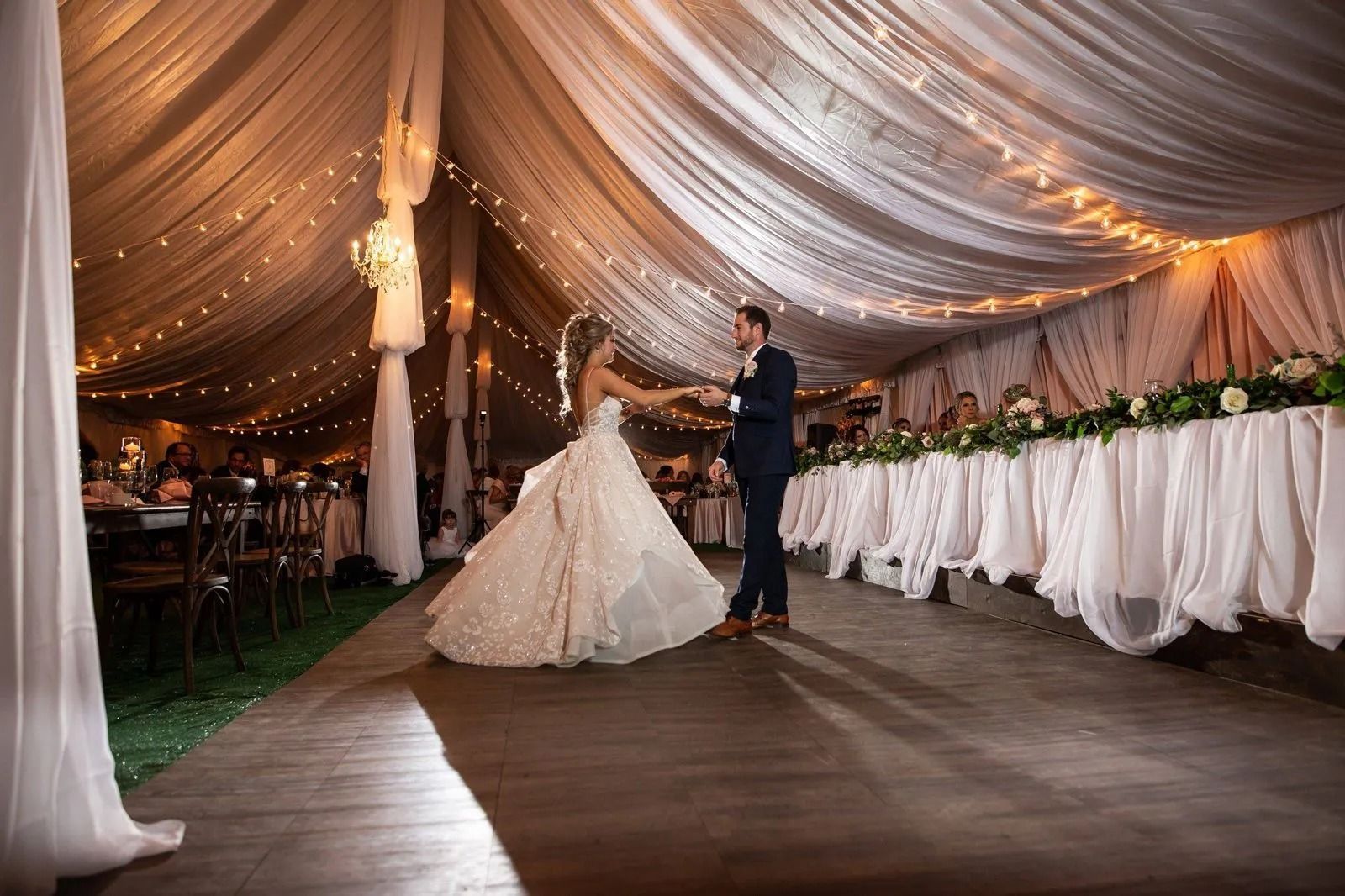 Bride and groom dancing at wedding reception. Tent decorated with string lights and white draping.