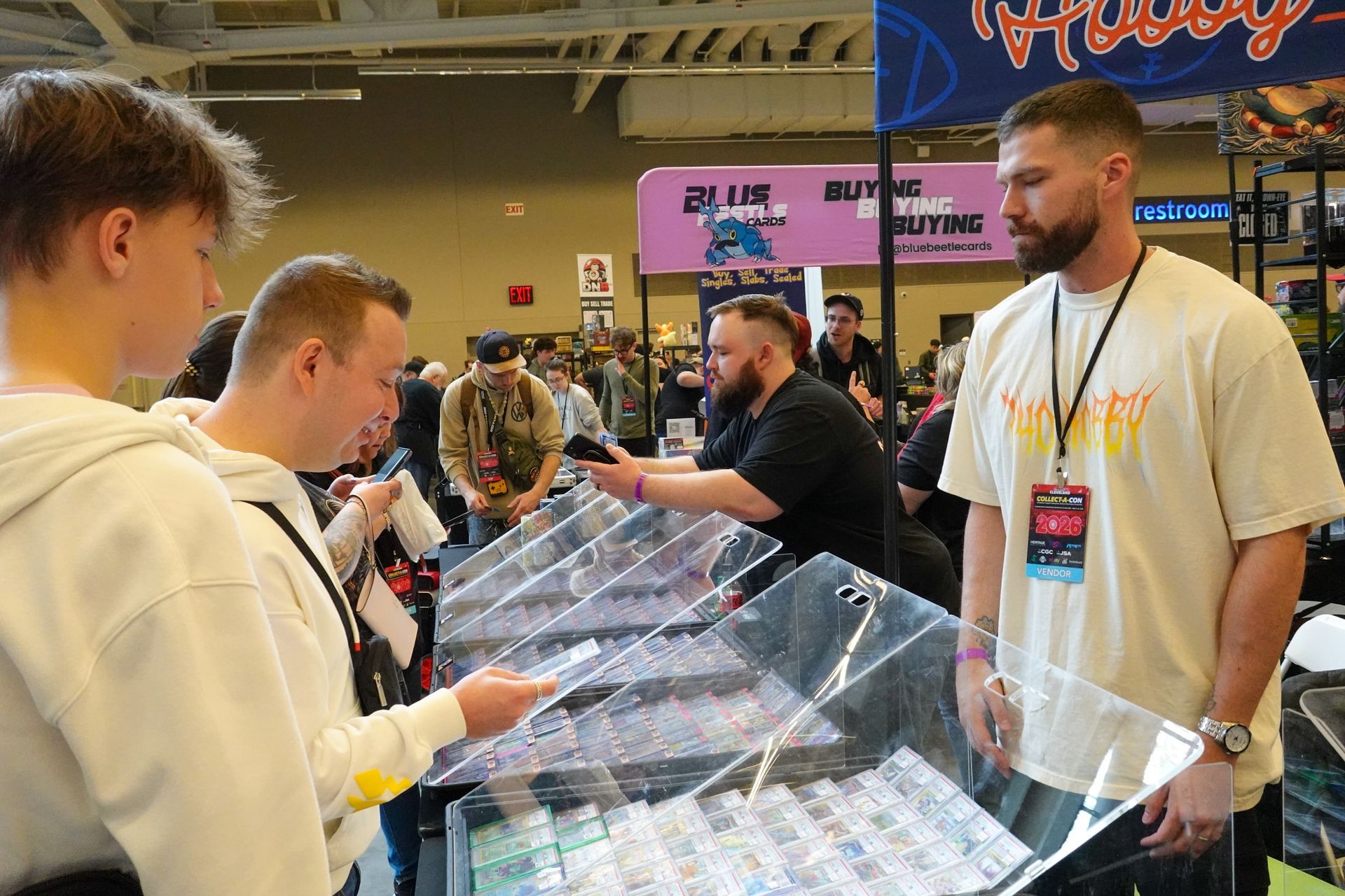 People browsing a card display at a busy indoor convention booth.