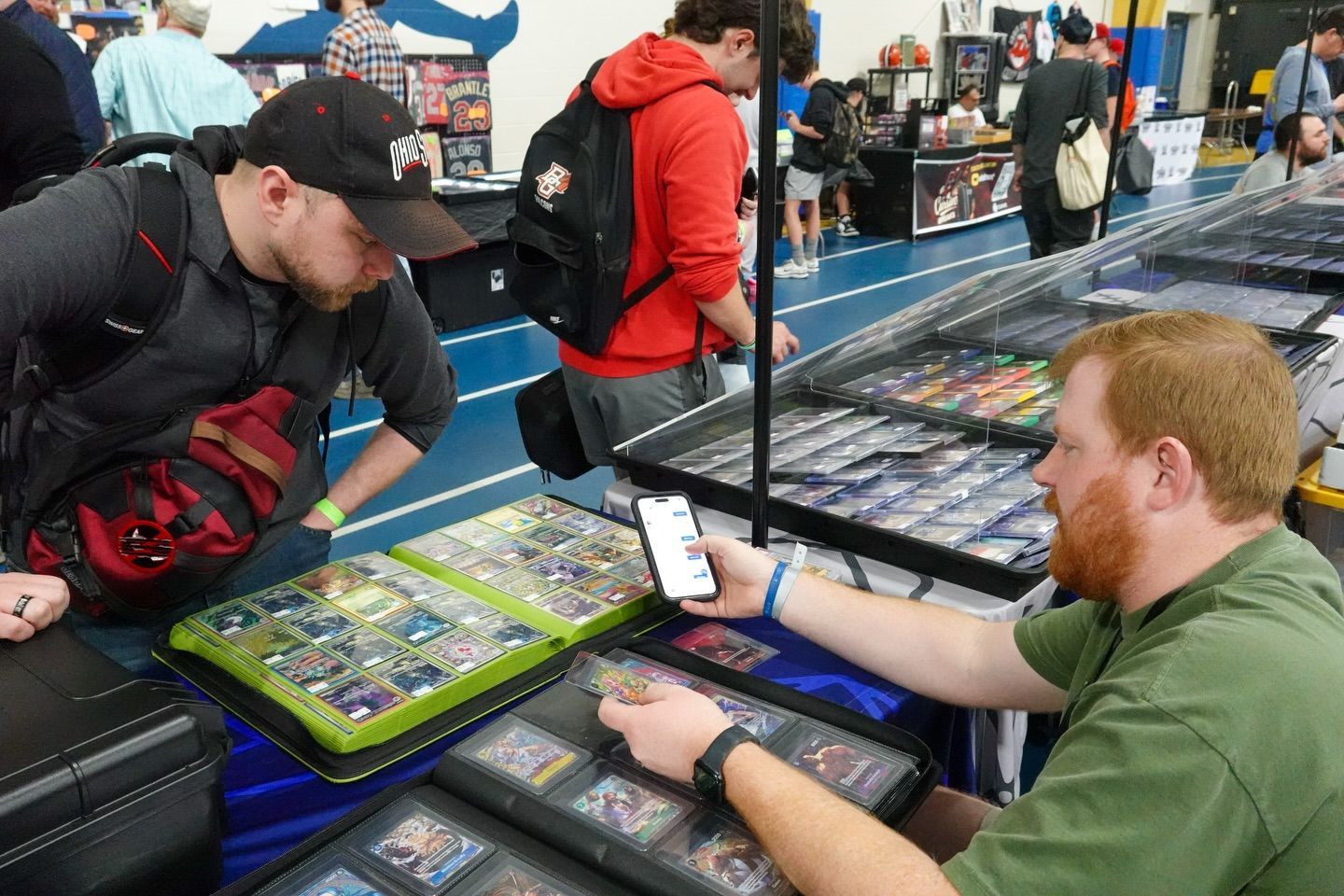 People browsing a crowded trading card convention, with one man holding up a card for another to see