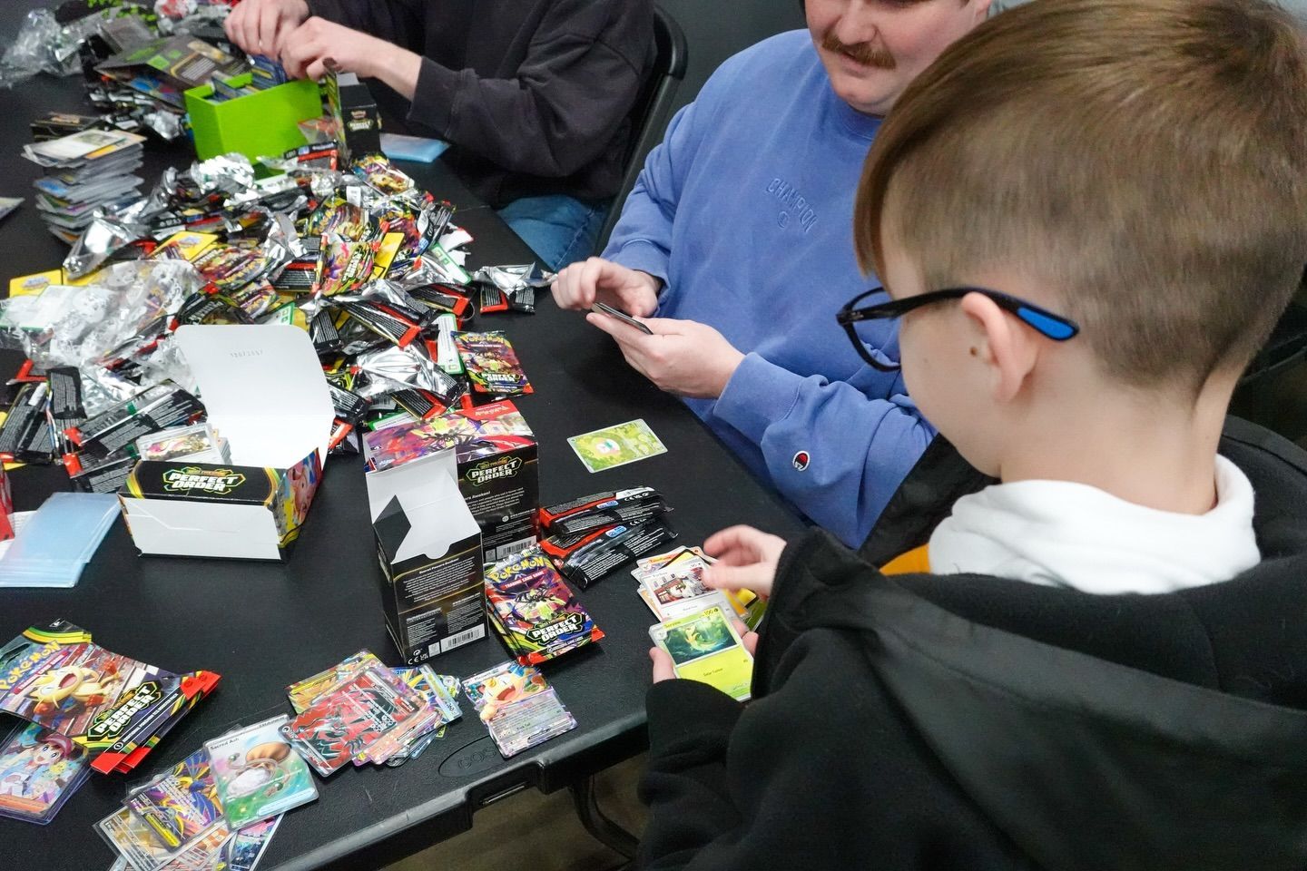 People sorting assorted trading card packs at a crowded table