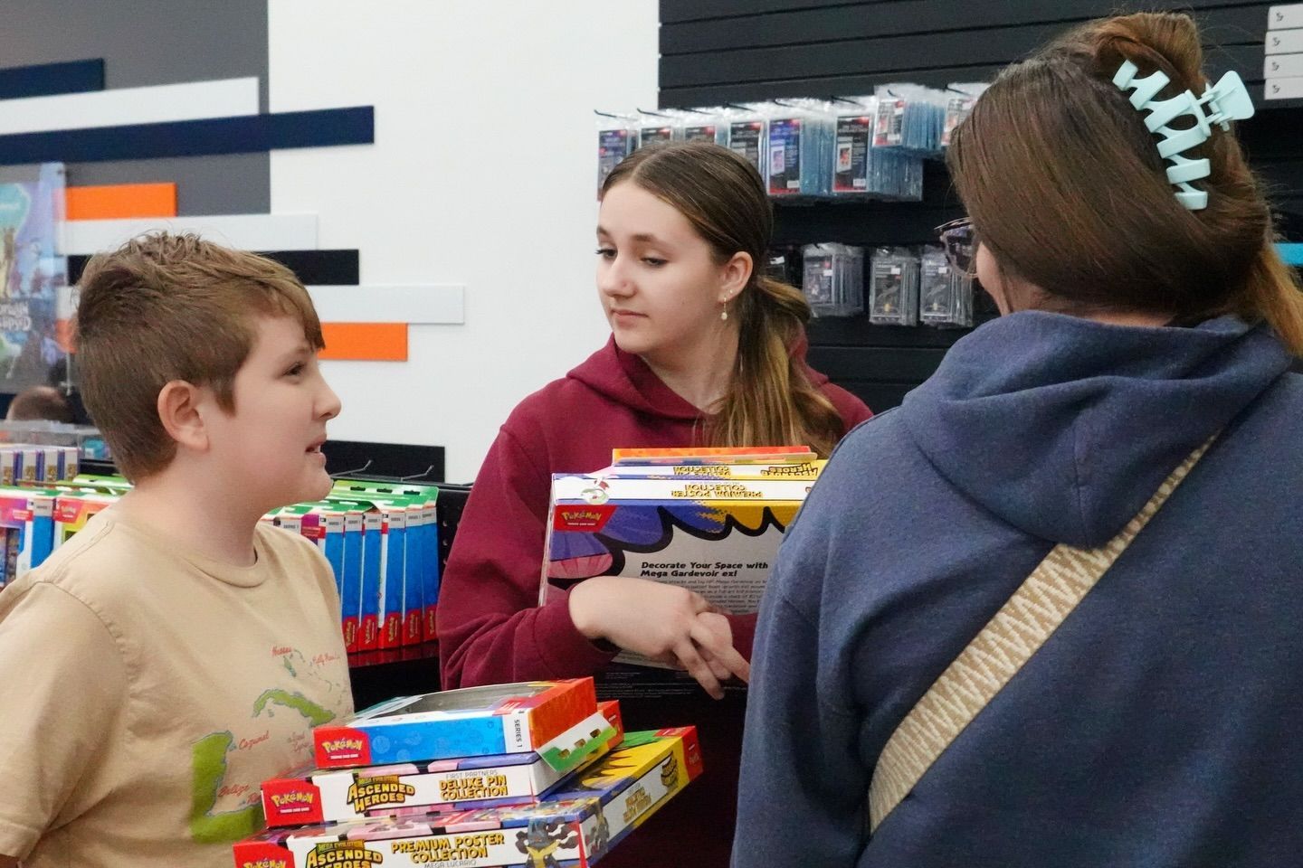 Three people browsing toys in a store aisle, with boxed games and colorful shelves in the background.