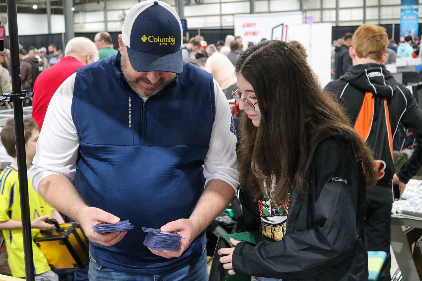 Two people in a crowded convention hall look at cards together.