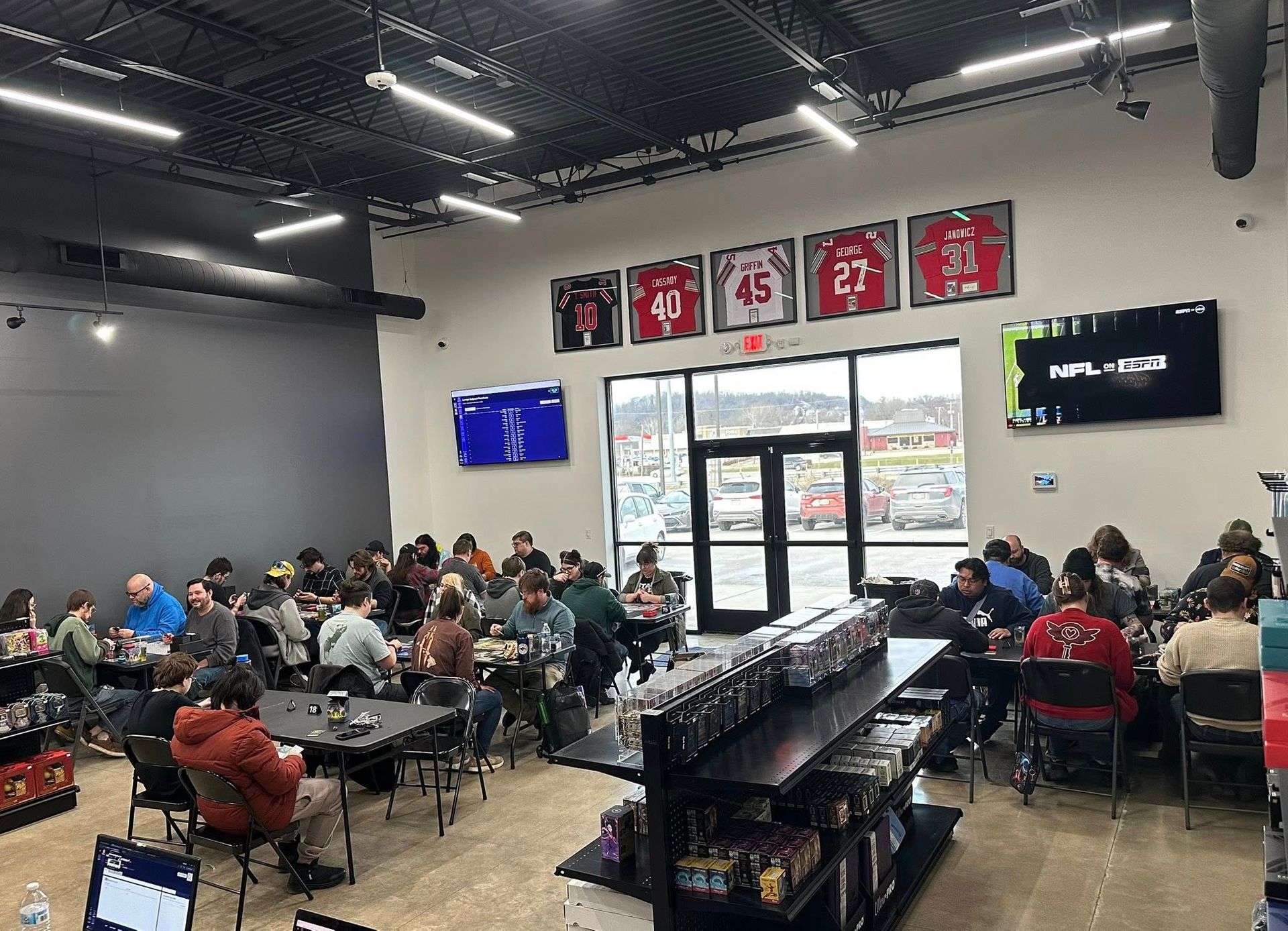 People seated at tables in a cafeteria with TV screens and sports jerseys on the wall.