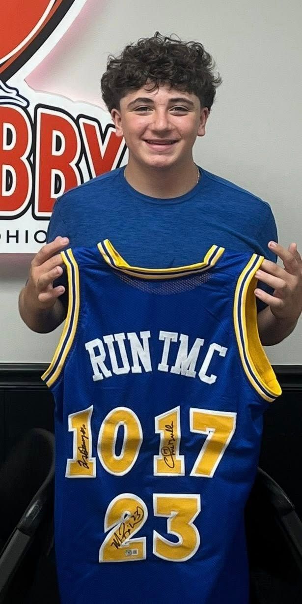 Smiling person holding a blue and yellow basketball jersey with “RUN TMC,” 1017, and 23 printed on it