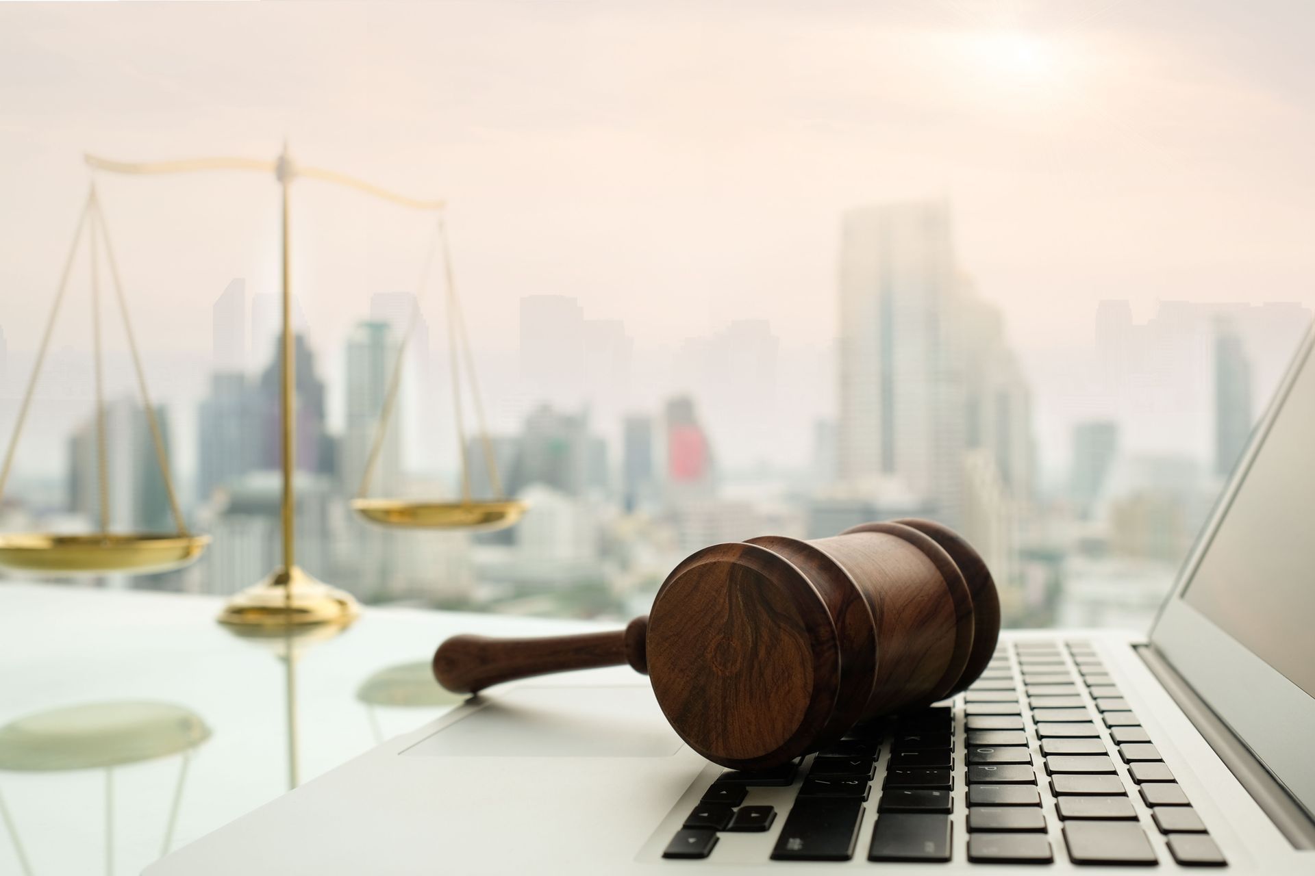 Scales of justice, gavel, and laptop on a table with cityscape background.