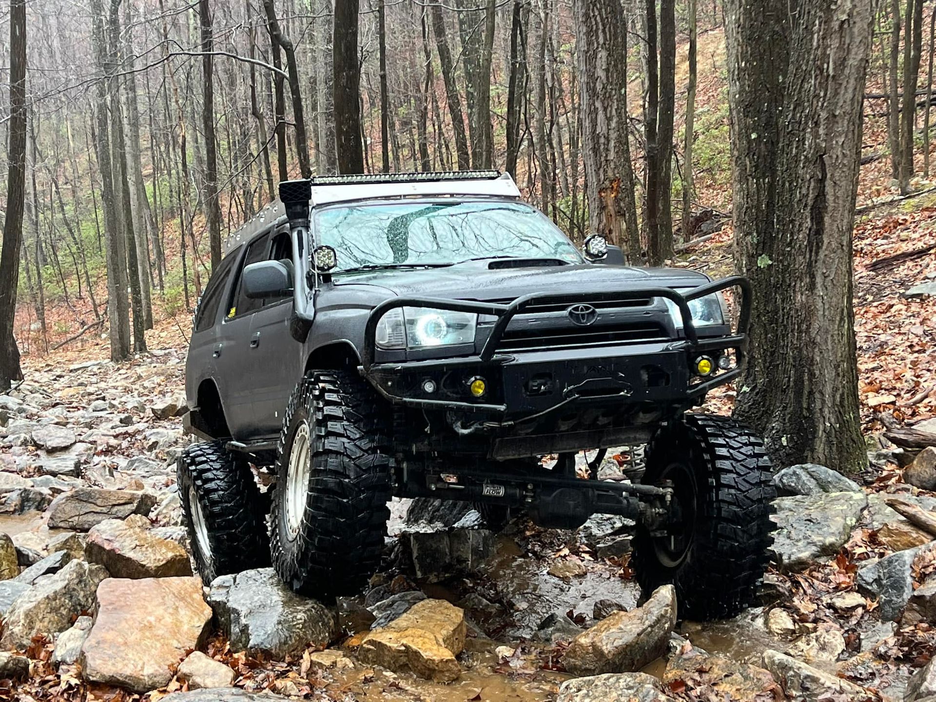 A black truck is driving through a rocky area in the woods