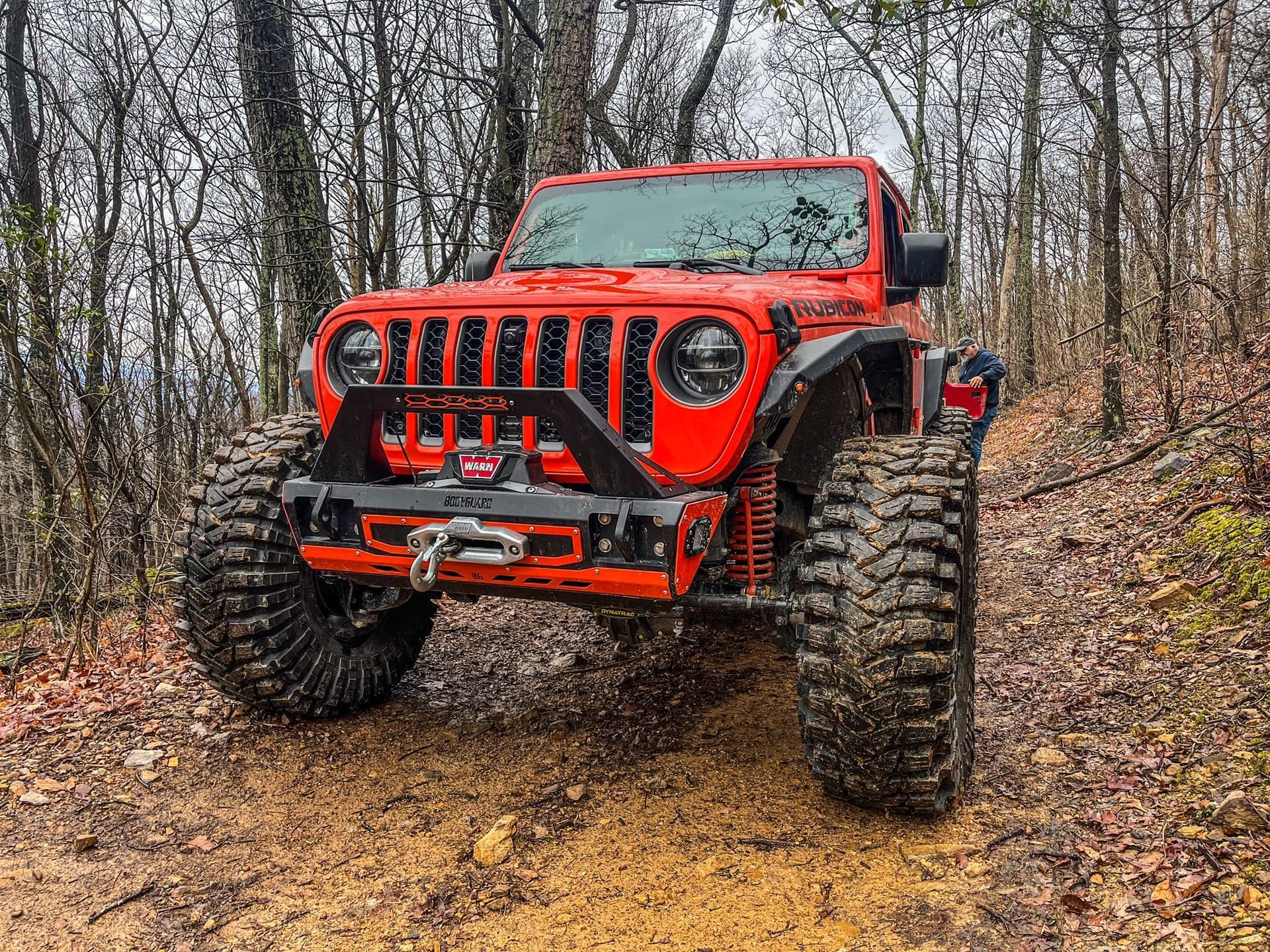 A red jeep parked on a dirt road in the woods