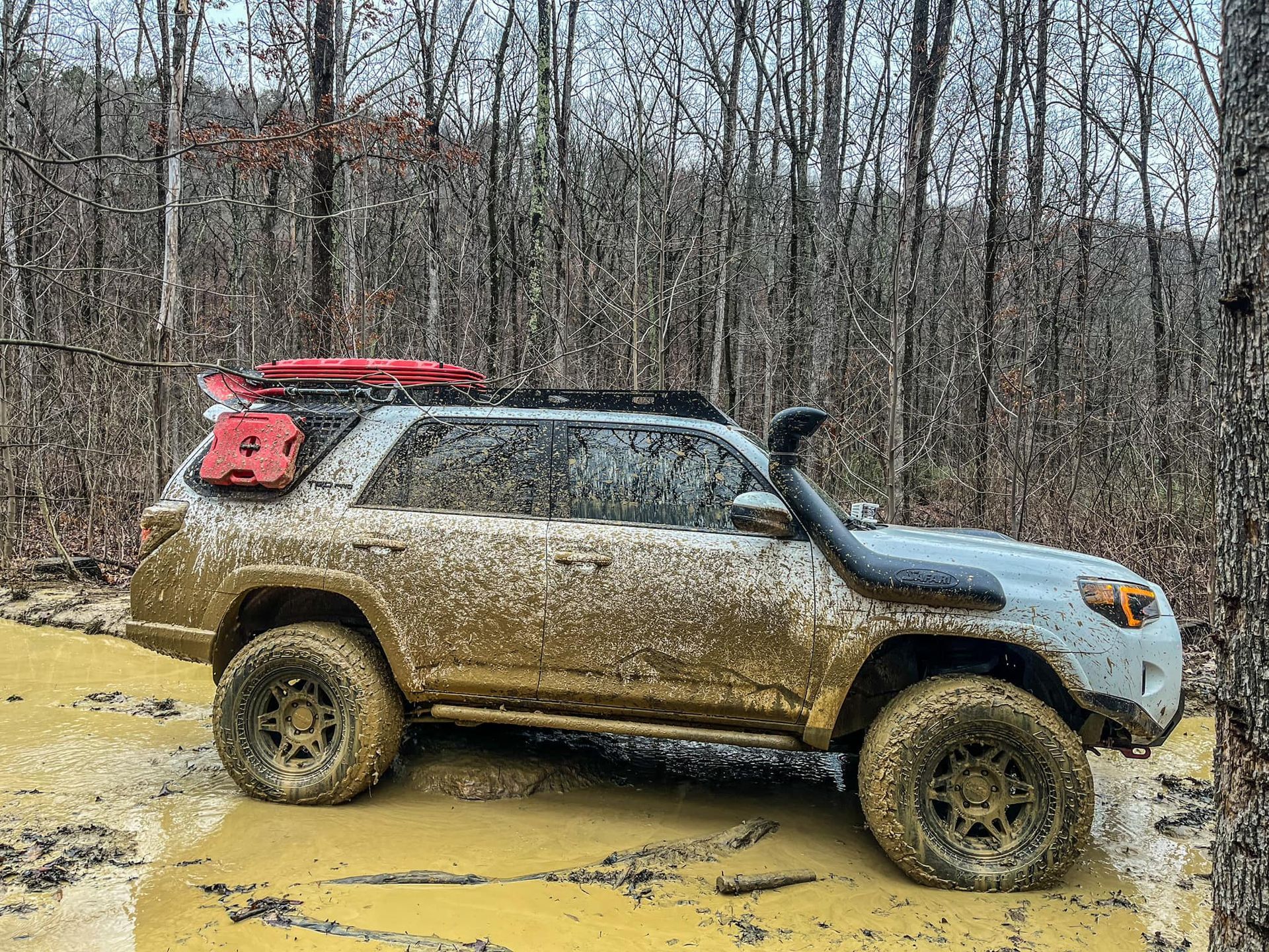 A muddy SUV driving down a muddy road in the woods