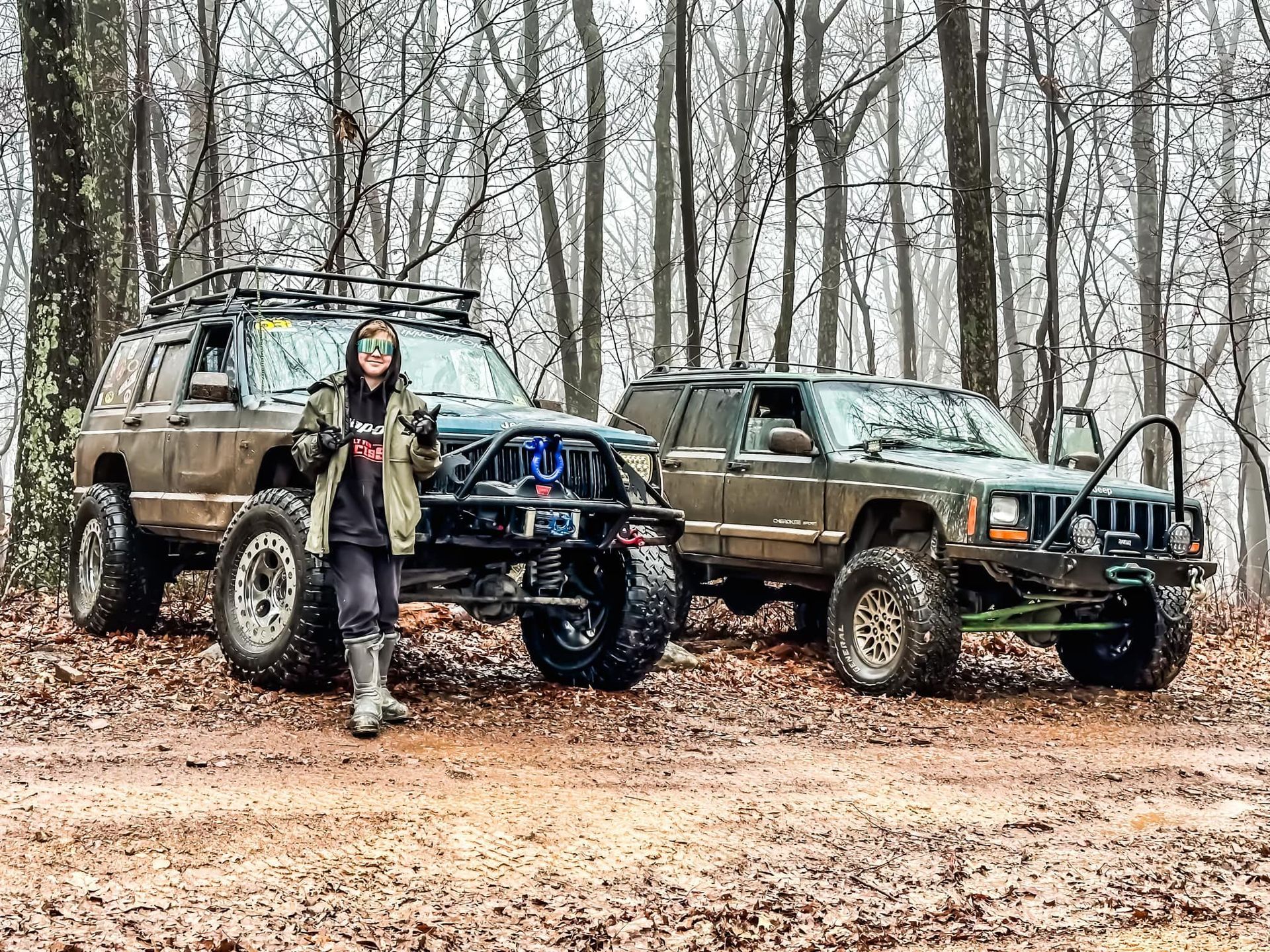 A woman standing next to two jeeps in the woods