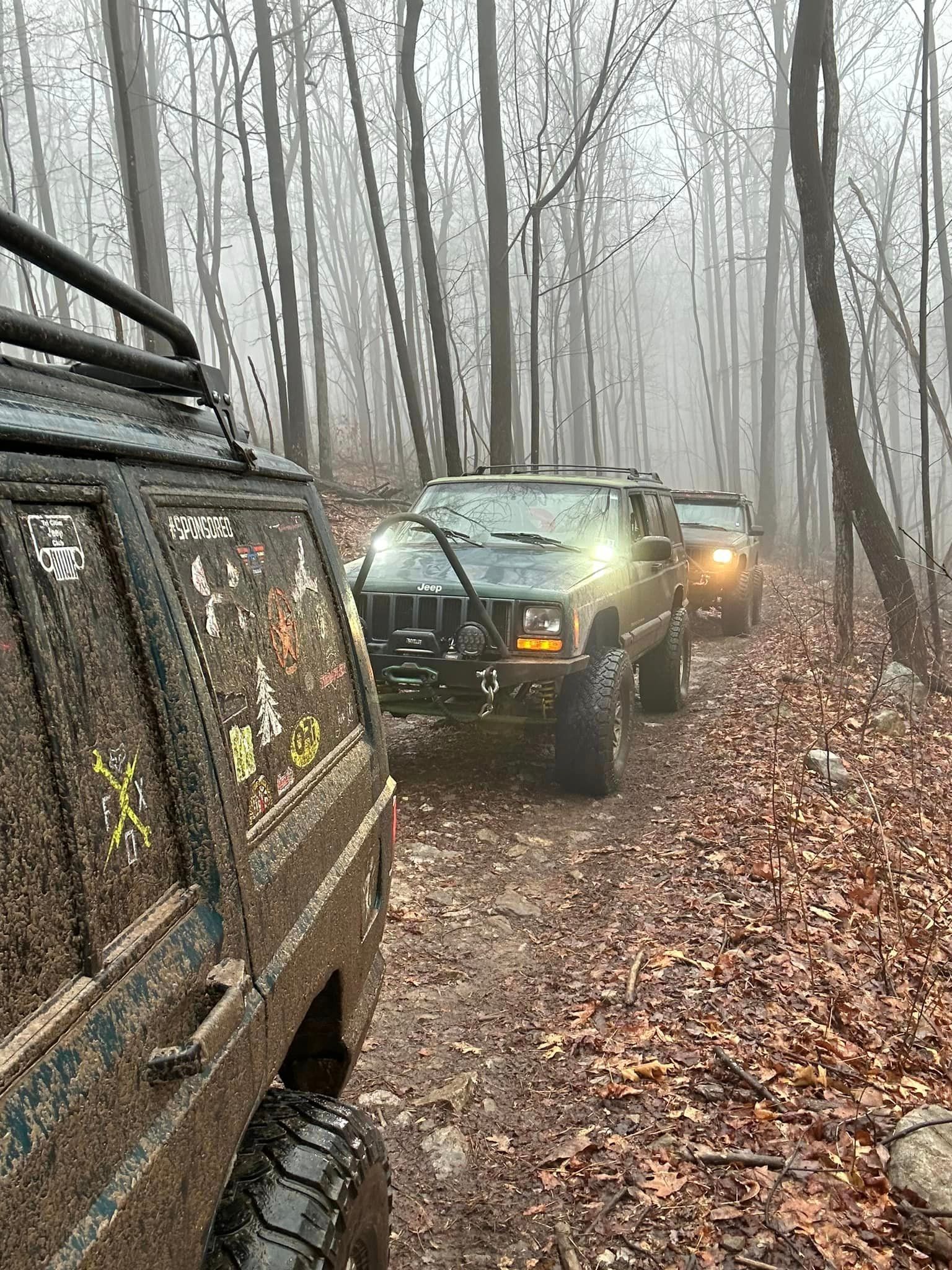 A group of jeeps driving down a dirt road in the woods