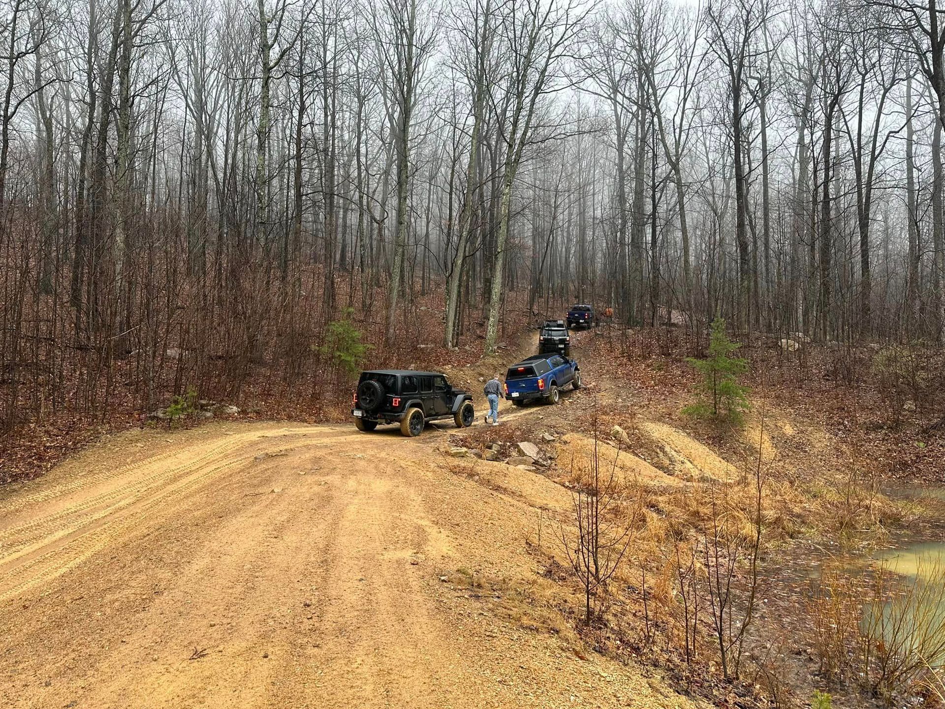 Two jeep parked on the side of a dirt road in the woods