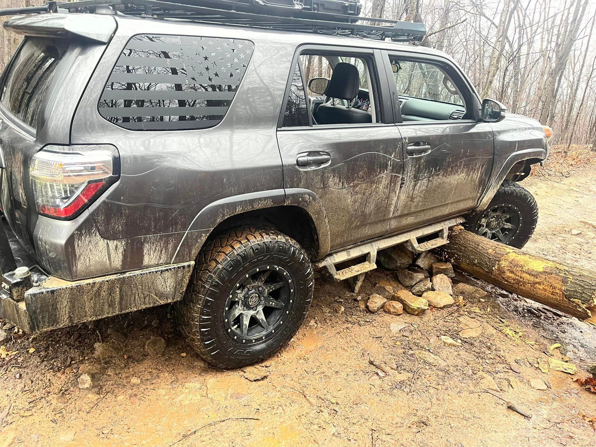 A muddy SUV parked next to a log in the dirt